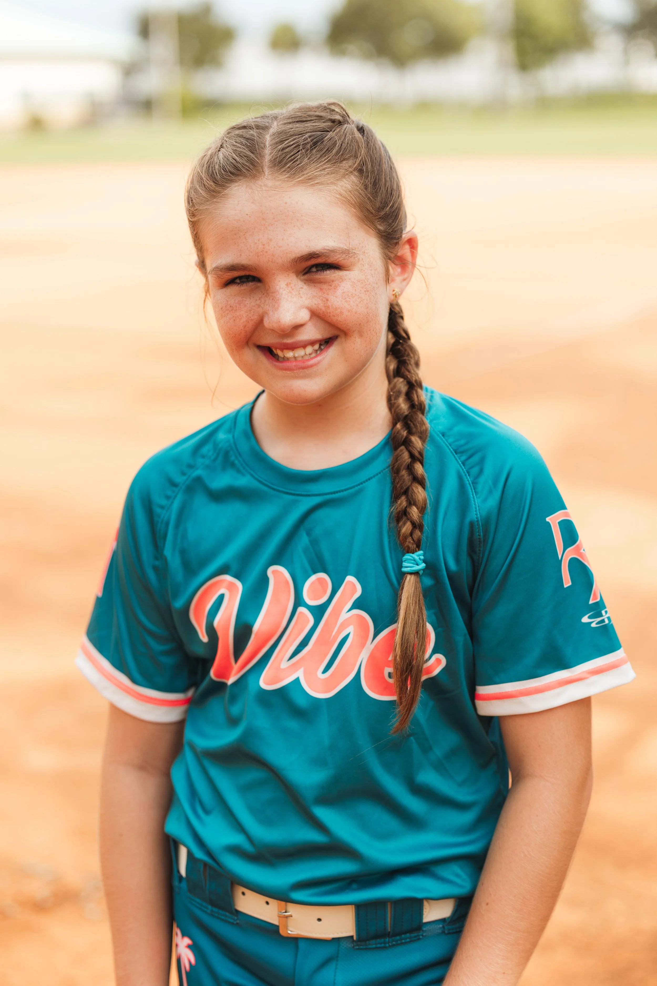 Claire, Vibe softball player number 7, smiles for a portrait in her teal uniform on the field.