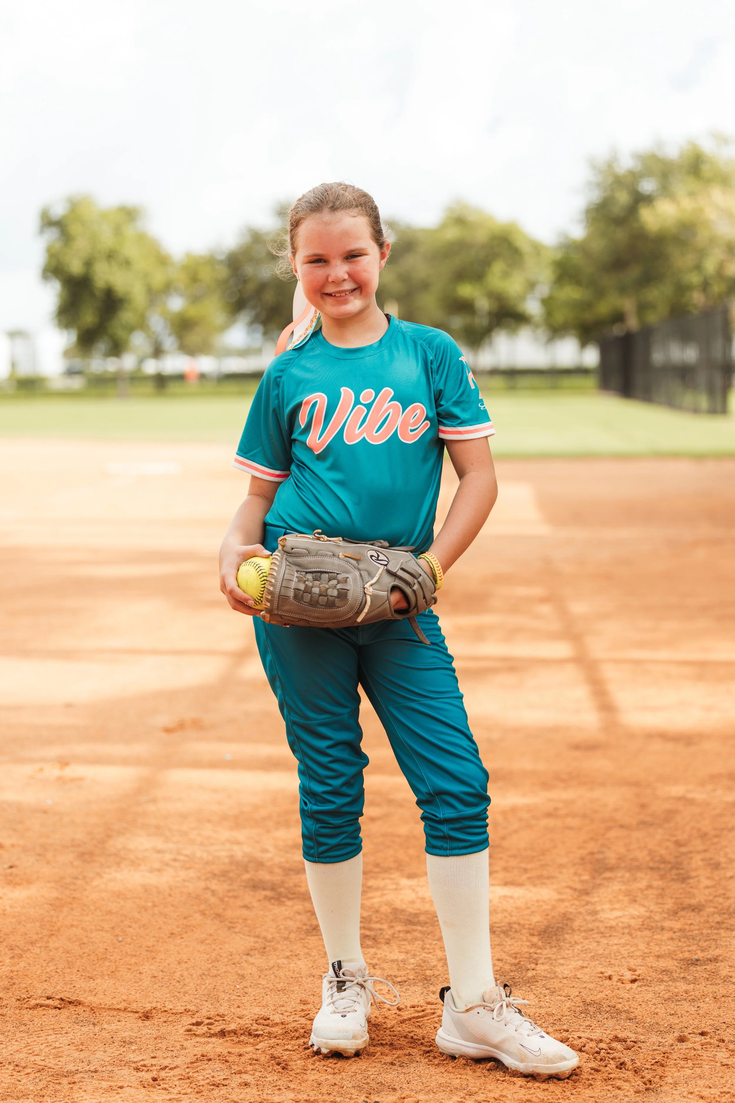 Blakely, Vibe softball player number 5, smiles on the infield while holding a softball and glove.