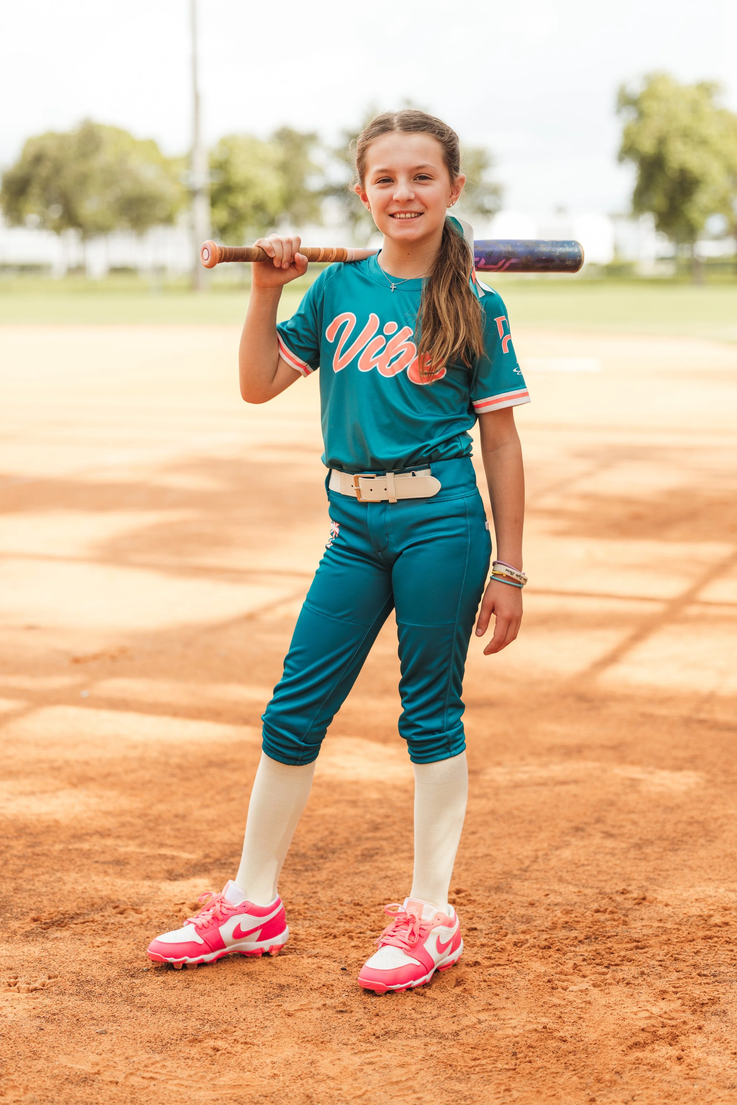 Maddie, Vibe softball player number 17, smiles on the infield with a bat resting across her shoulder.