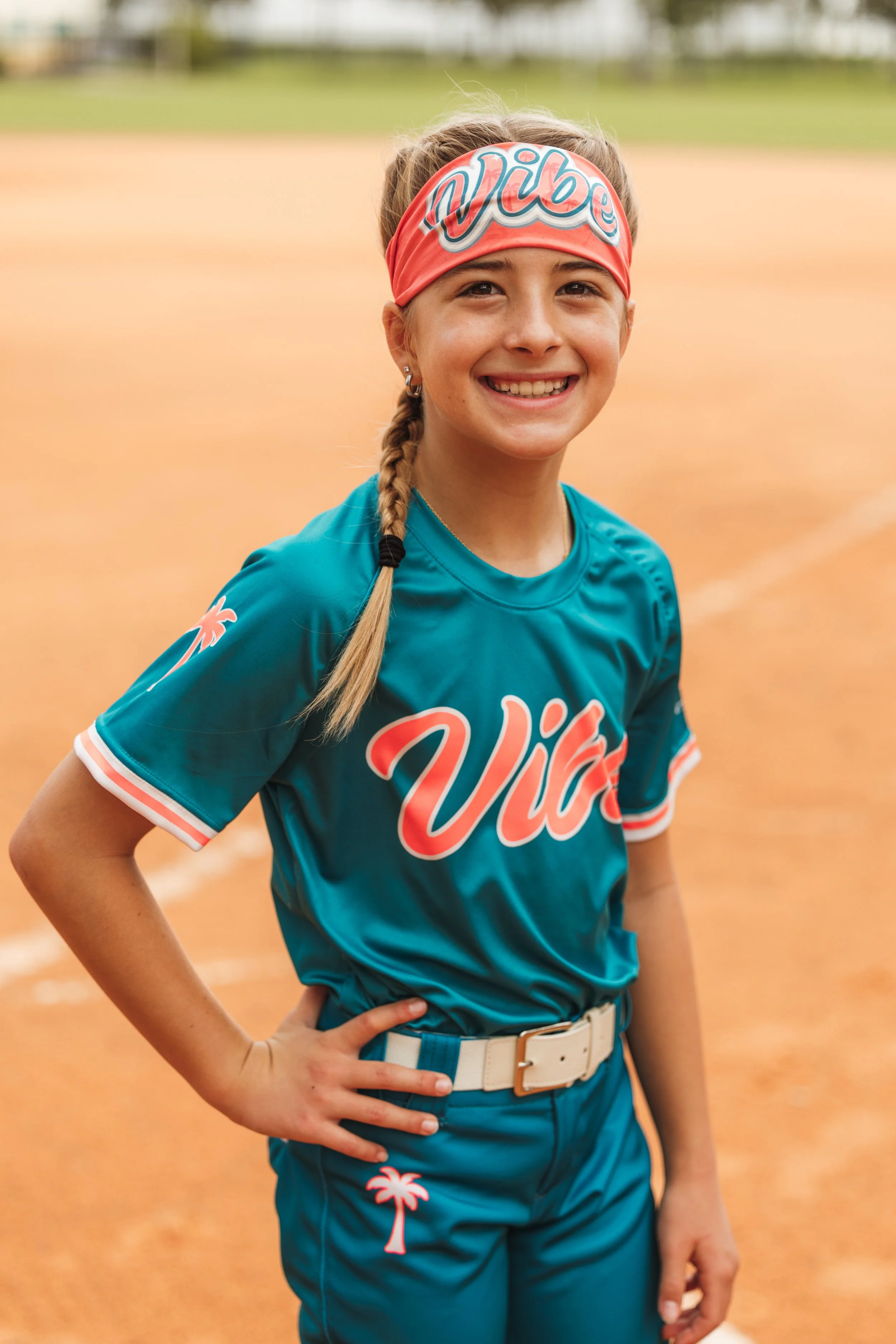 Taelyn, Vibe softball player number 18, smiles in her teal uniform and Vibe headband on the infield.