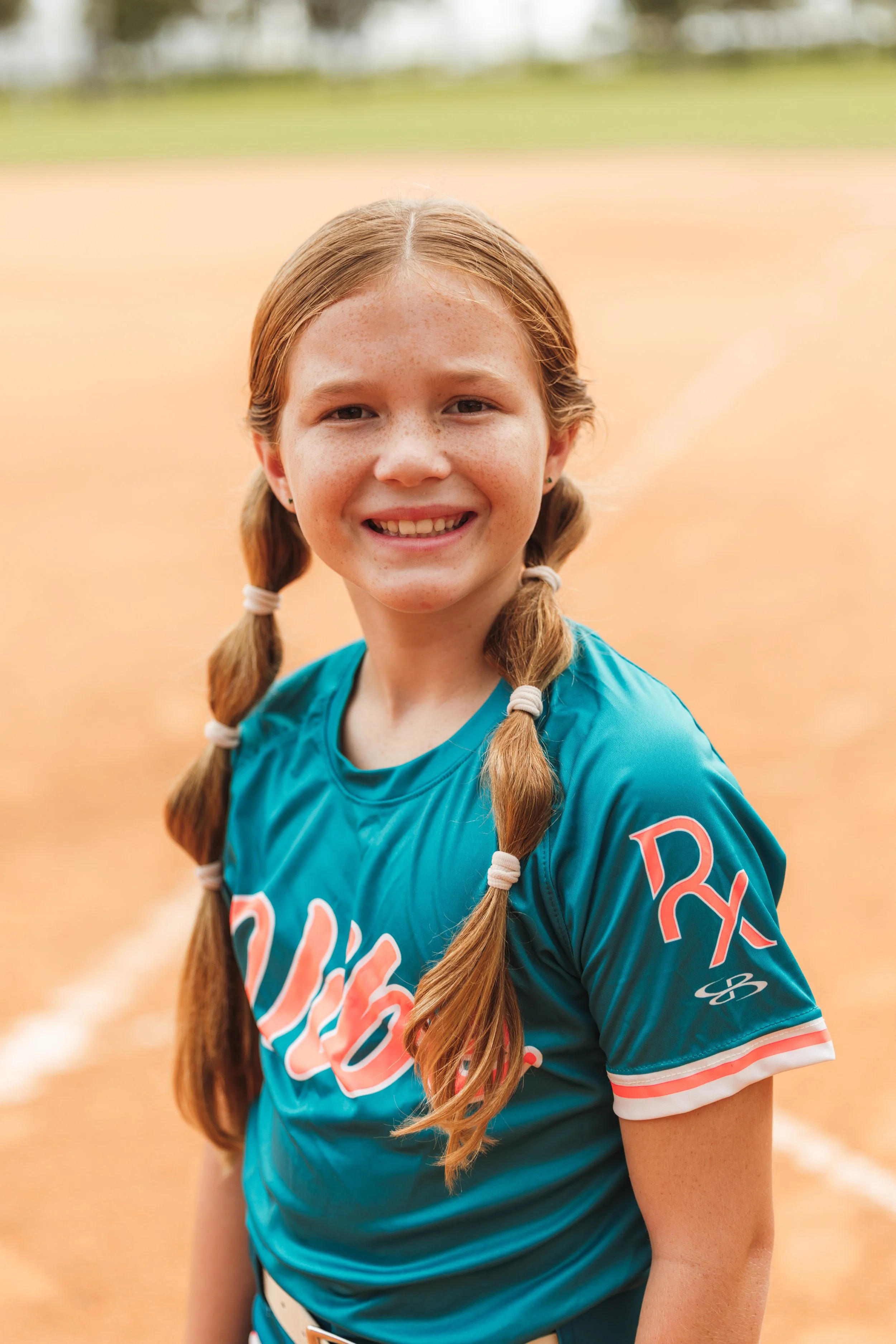 Bree, Vibe softball player number 2, smiles for a portrait in her teal uniform on the field.