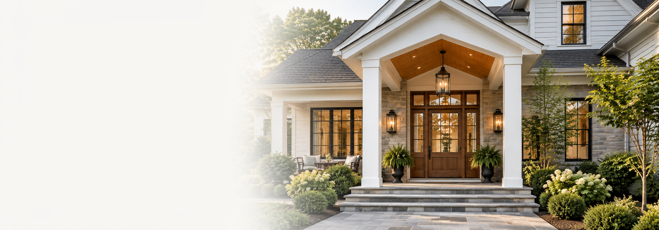 Elegant house with a front porch, wooden door, large windows, and landscaped garden with bushes and small trees.