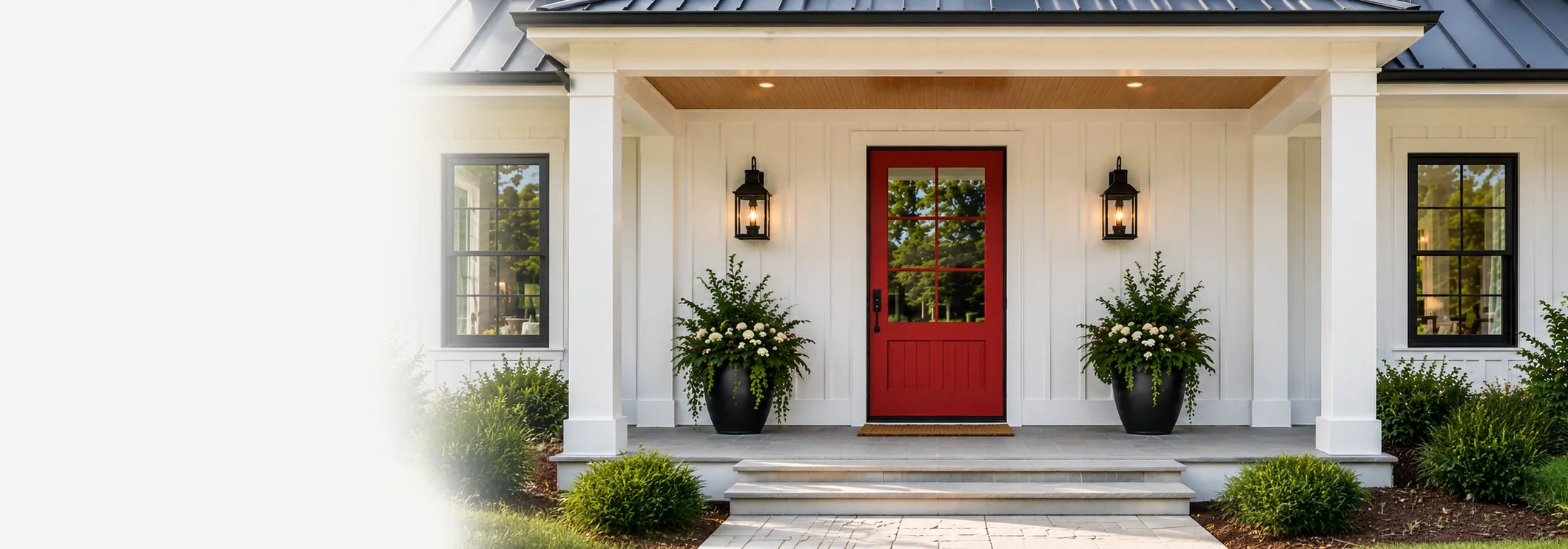 Front porch of a house with a red door, black lanterns on either side, potted plants, and steps leading up to it.