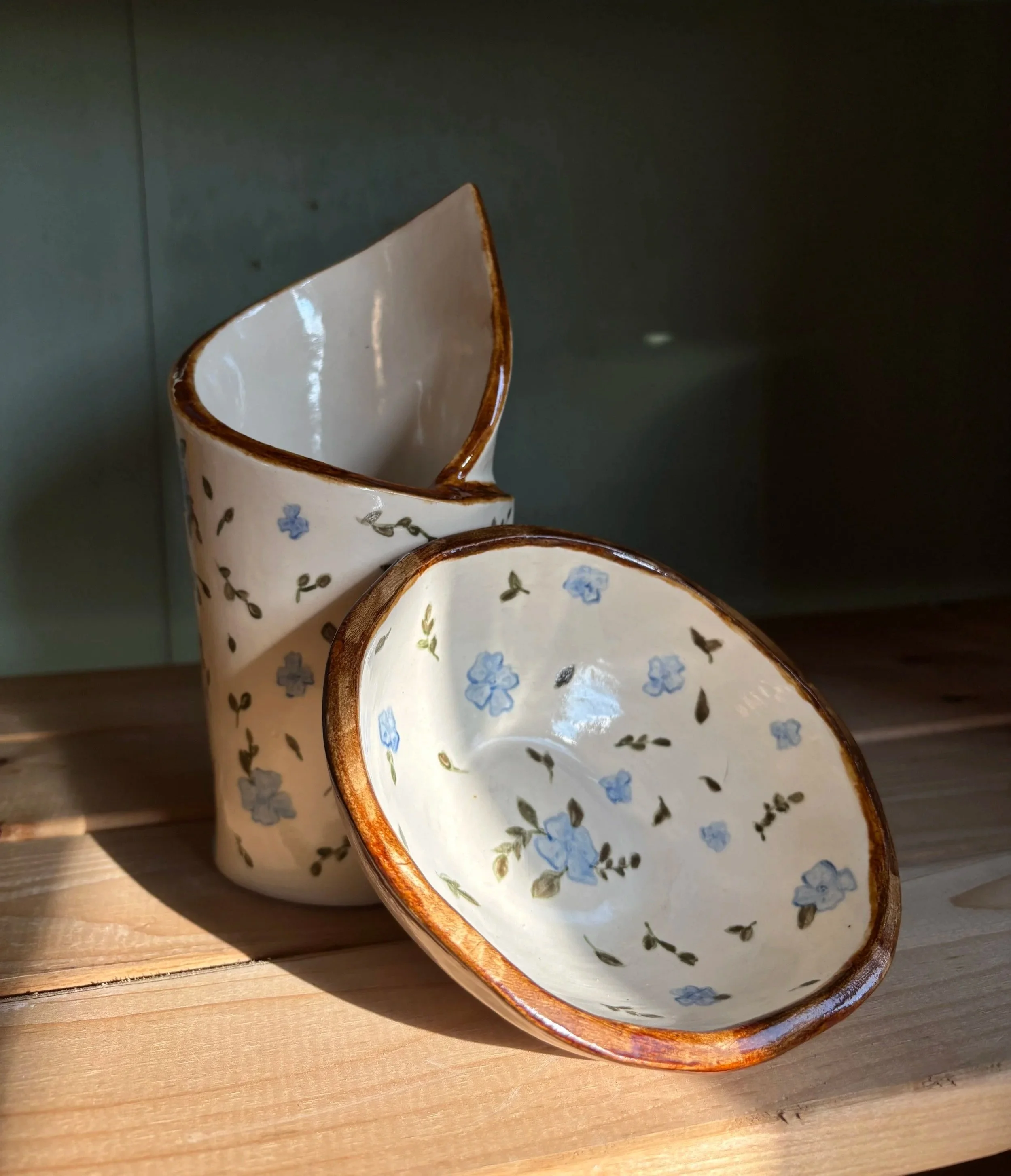Two ceramic cups with floral patterns and copper-colored rims, placed on a wooden surface, with a dark background.