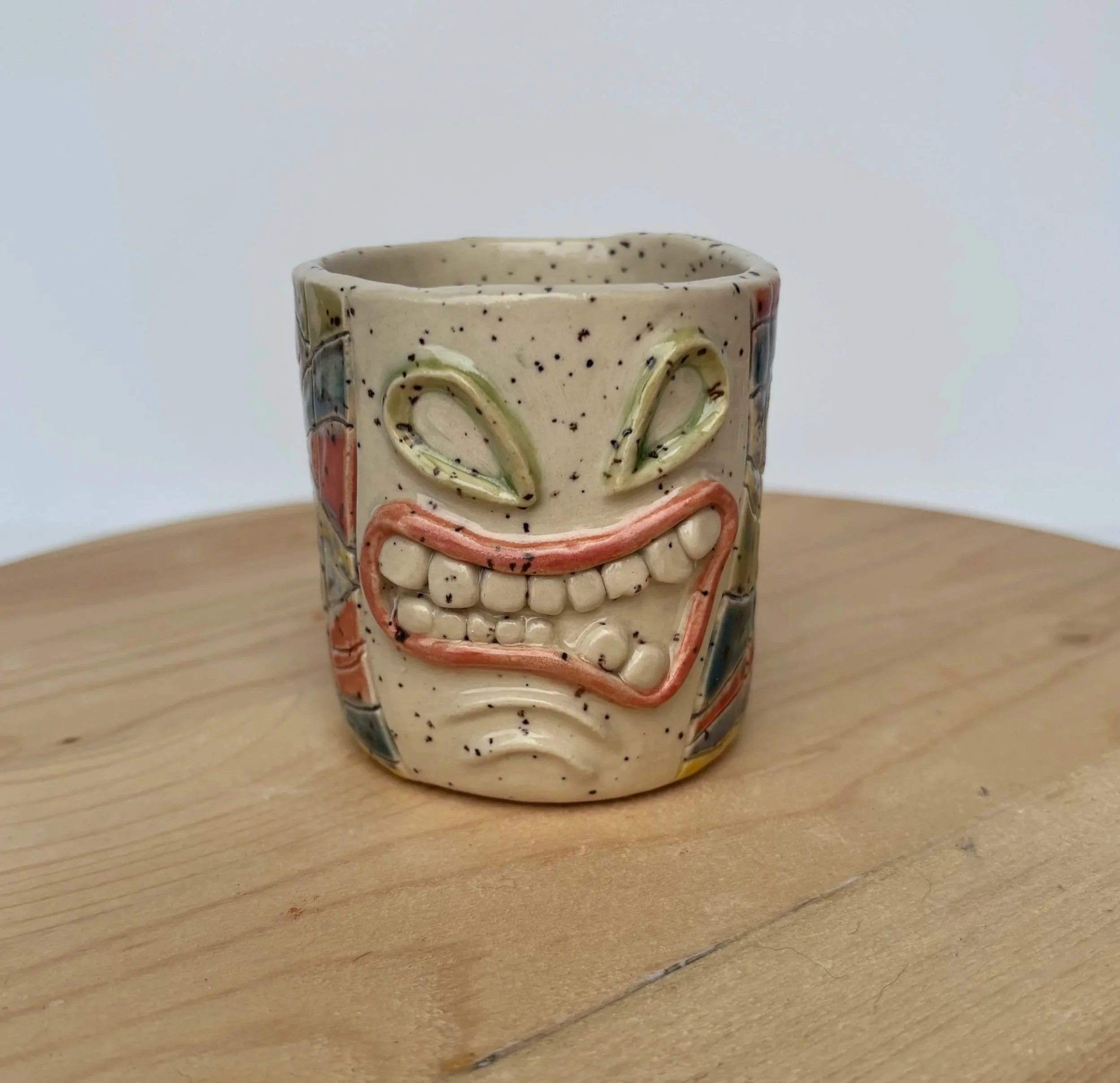 A ceramic mug with a cream-colored background, decorated with colorful and abstract floral patterns, placed on a wooden surface.
