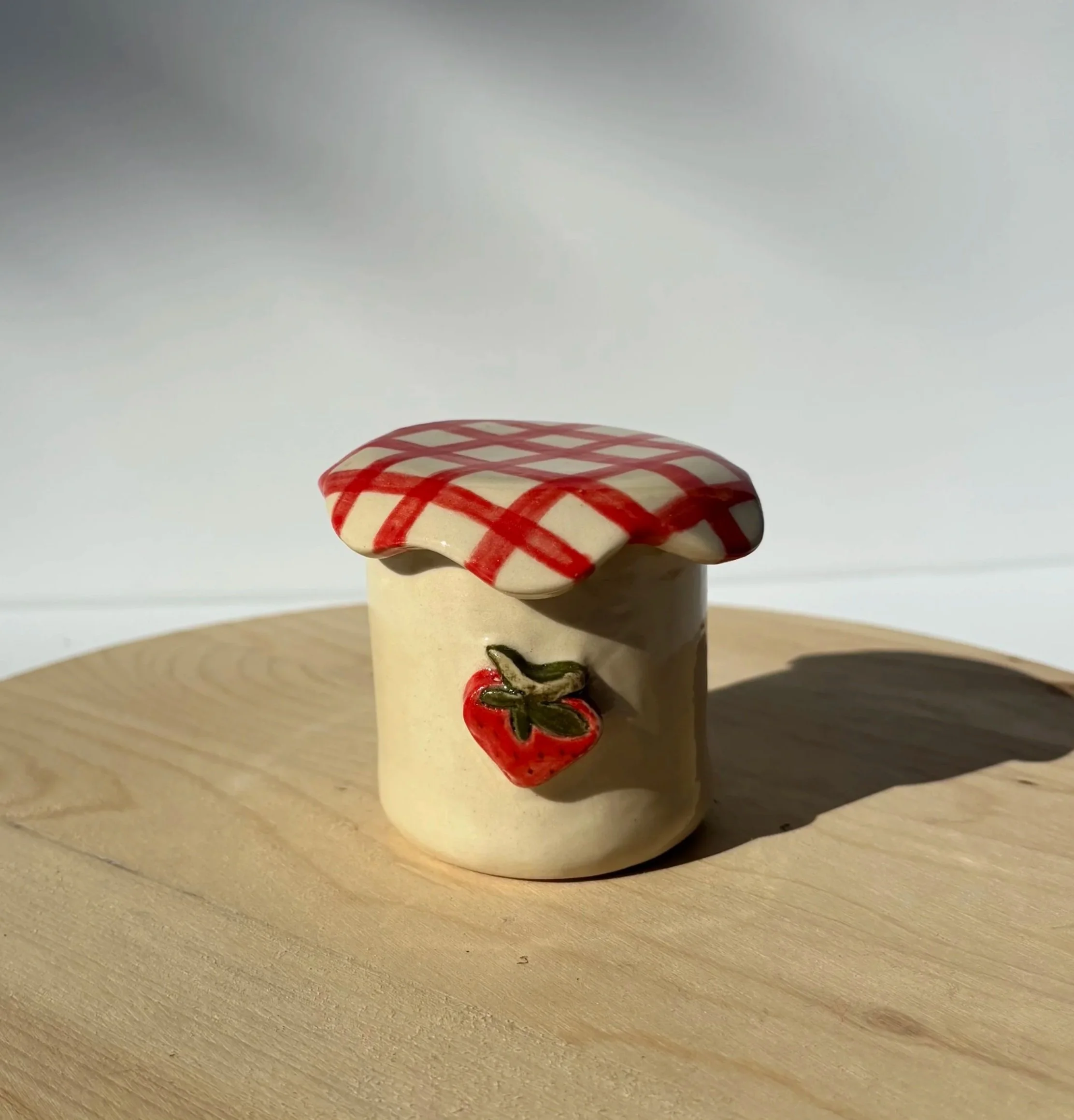 Close-up of a ceramic figurine resembling a mushroom with a red and white checkered cap, placed on a wooden surface against a plain background.