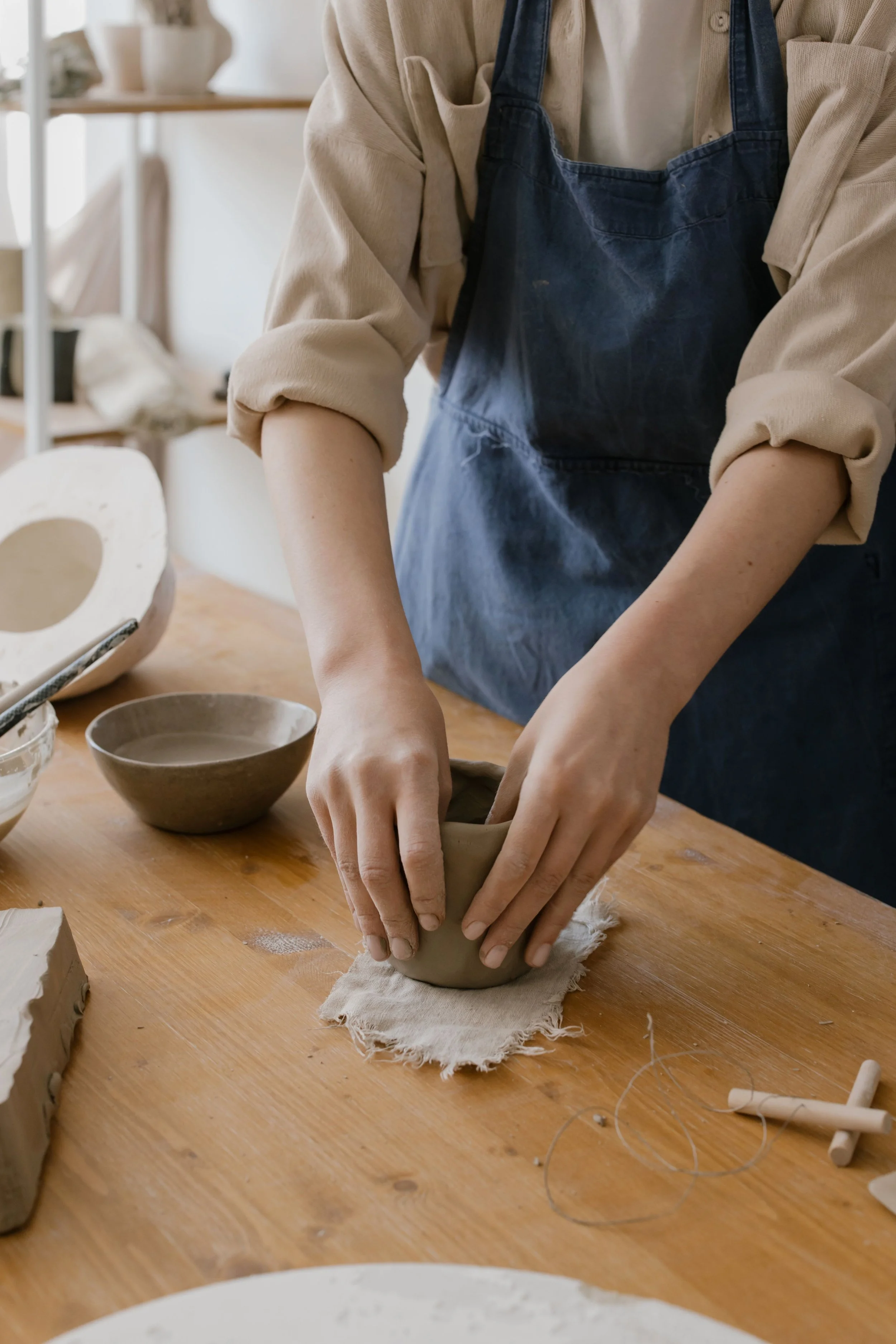 Person shaping clay on a pottery wheel in a studio.