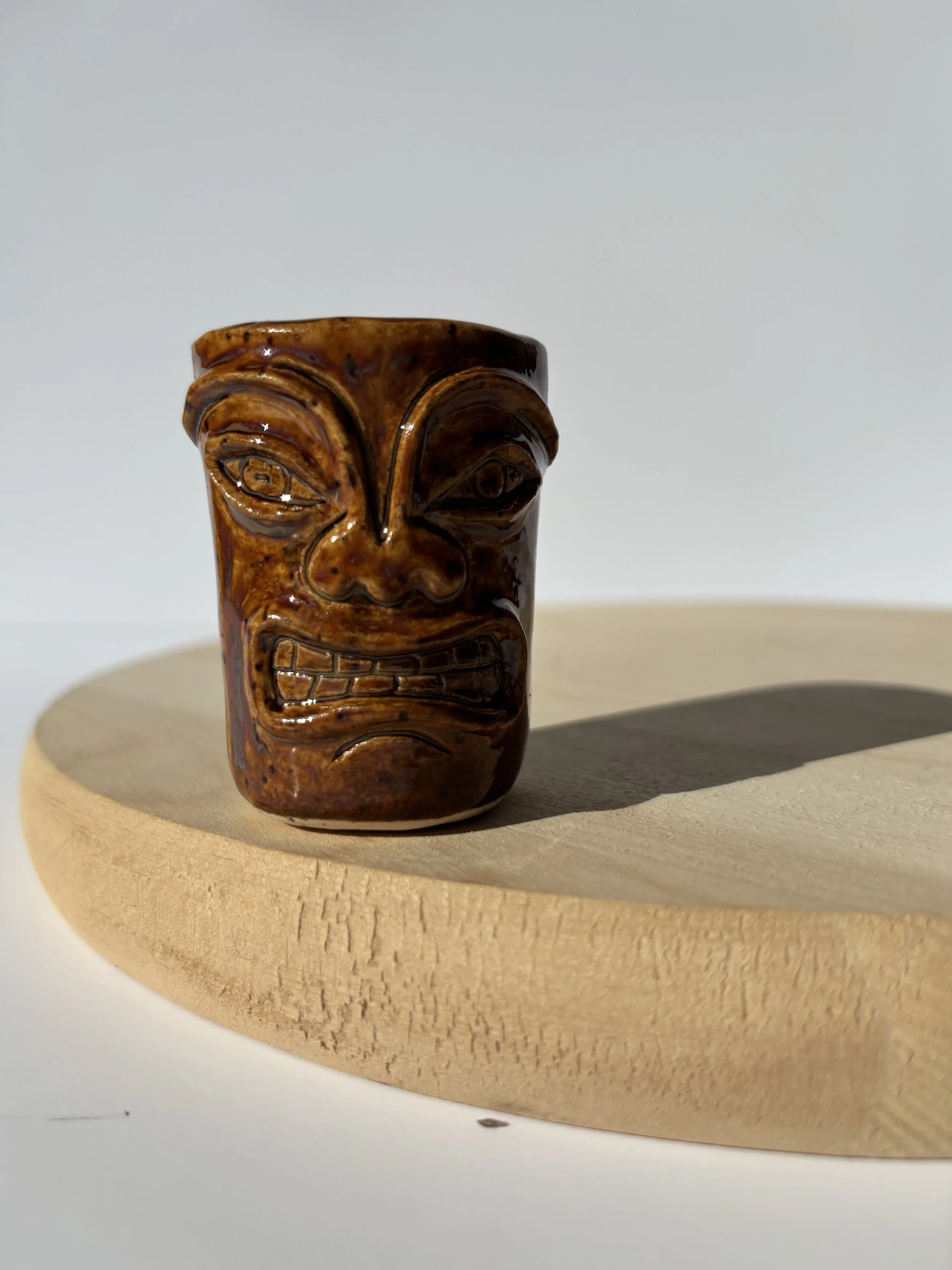 A carved wooden tiki figure with exaggerated facial features, resting on a round wooden surface.
