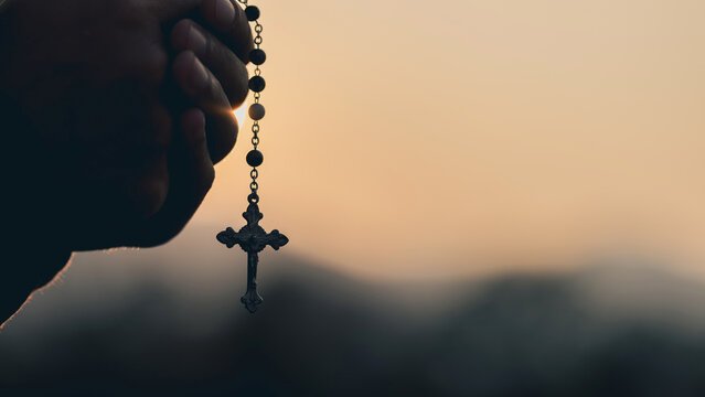 A person holding a rosary with a crucifix at sunset.