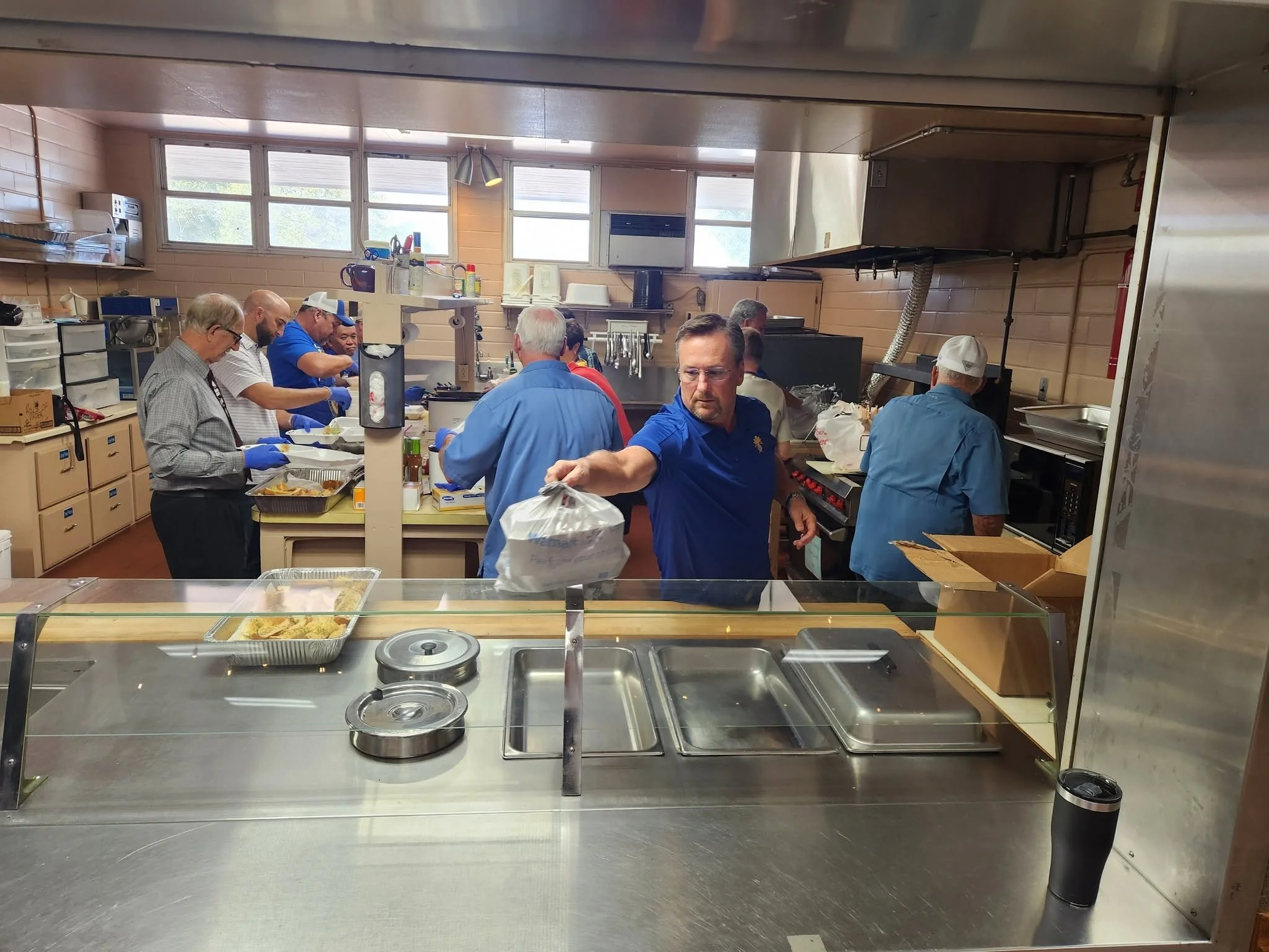 Kitchen with people preparing food, stainless steel counters, equipment, and storage shelves