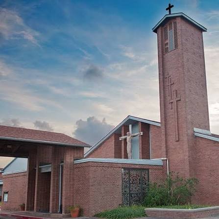 A brick church building with a tall steeple and a cross on top, featuring a crucifix with Jesus on the cross attached to the front of the church.
