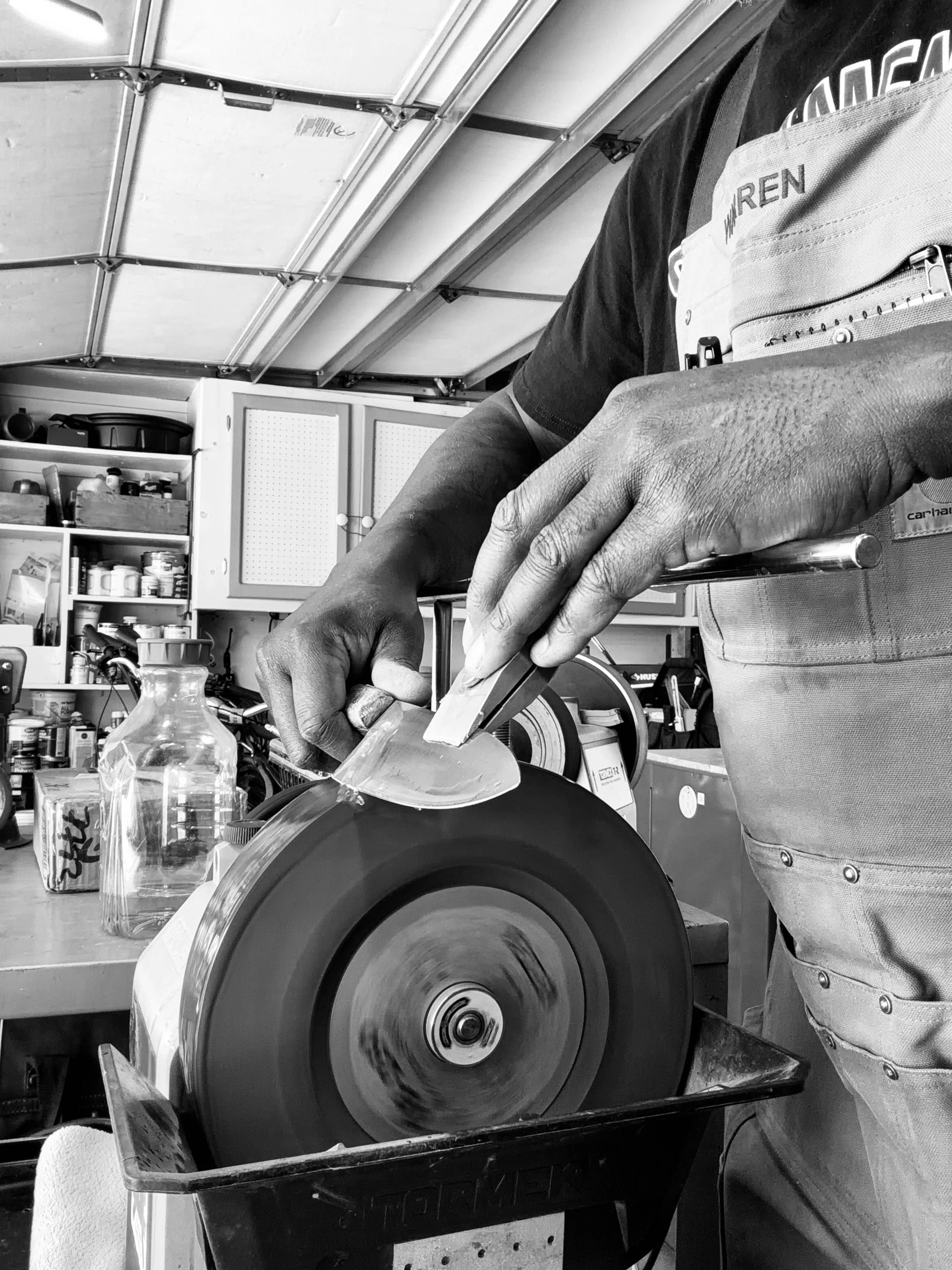 A person using a circular saw to cut a piece of wood in a workshop. The workshop has shelves with various tools and supplies in the background.