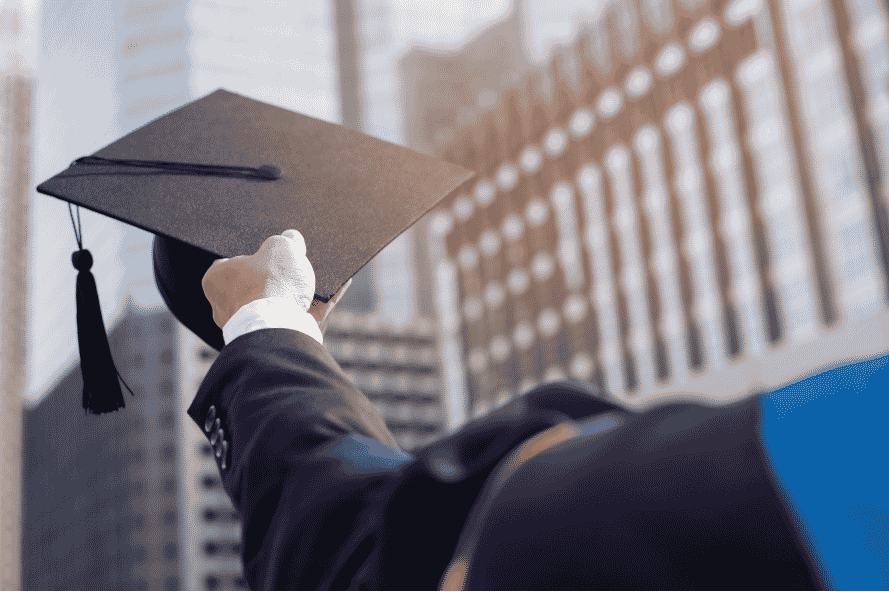 A person holding a graduation cap towards a horizon of city buildings.