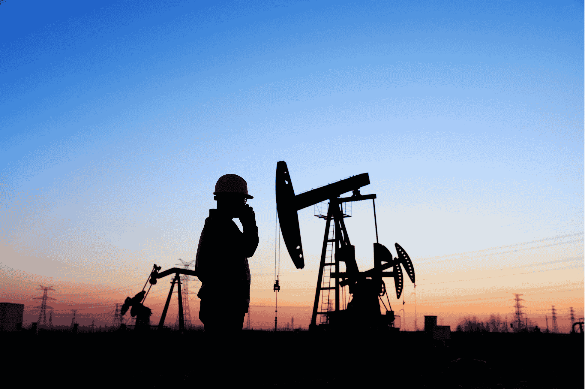 In the foreground is the silhouette of an oil worker. In the background there are silhouettes of oil rigs and electric power lines.