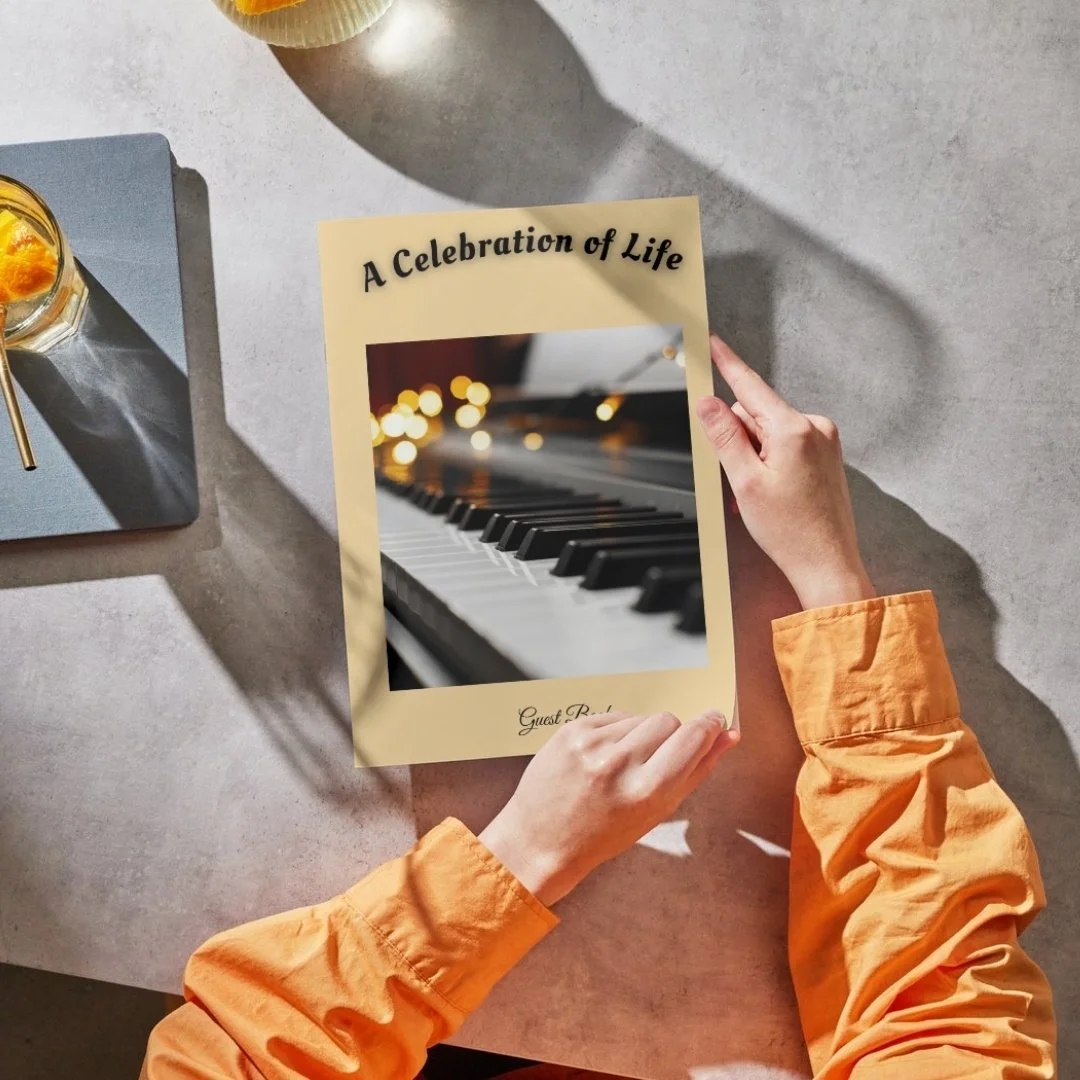 A person in an orange jacket is holding a beige card with a photo of piano keys and blurred lights, titled 'A Celebration of Life'.