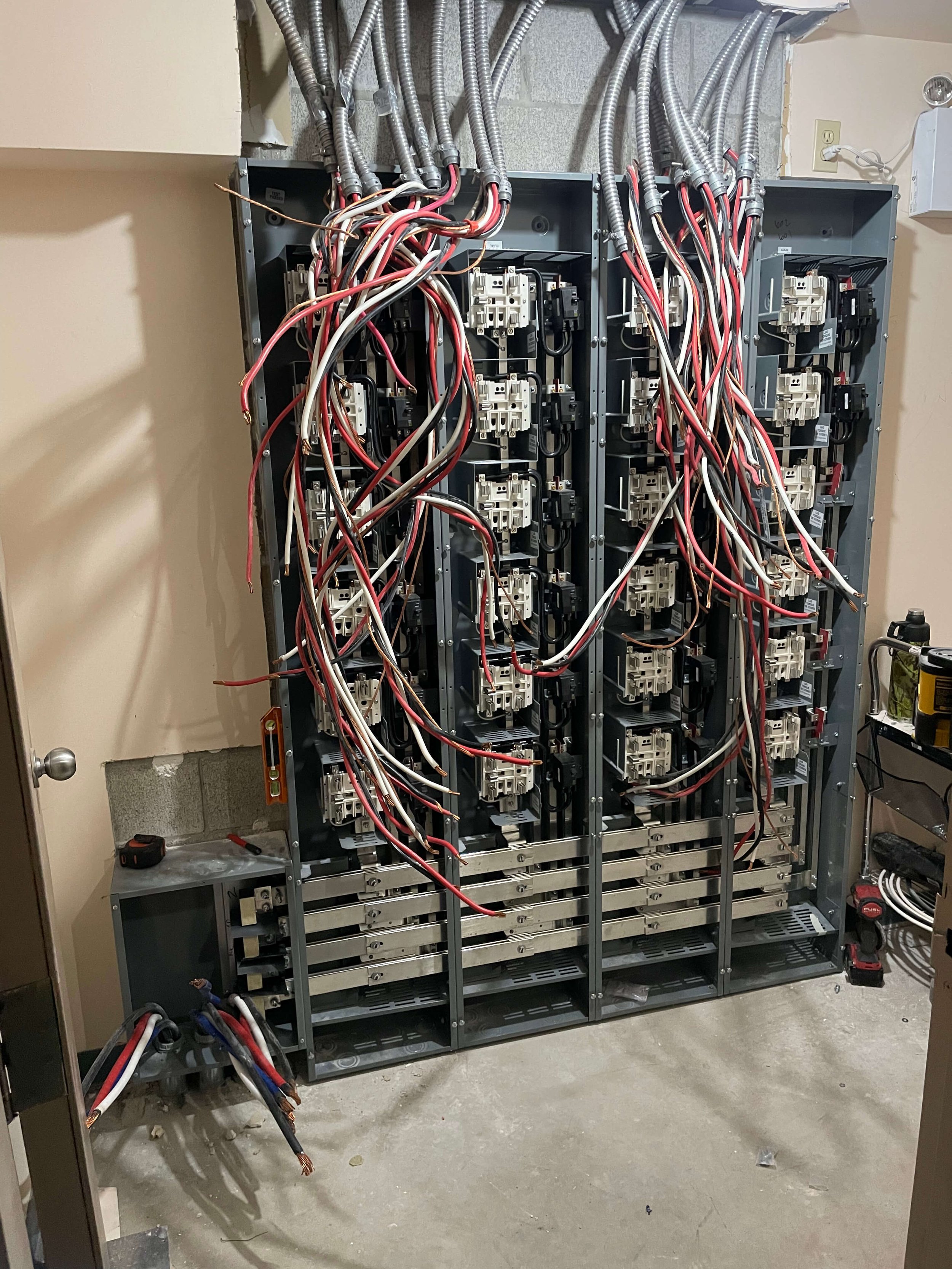 Open electrical panel with numerous wires and circuit breakers inside, ongoing electrical work in progress.