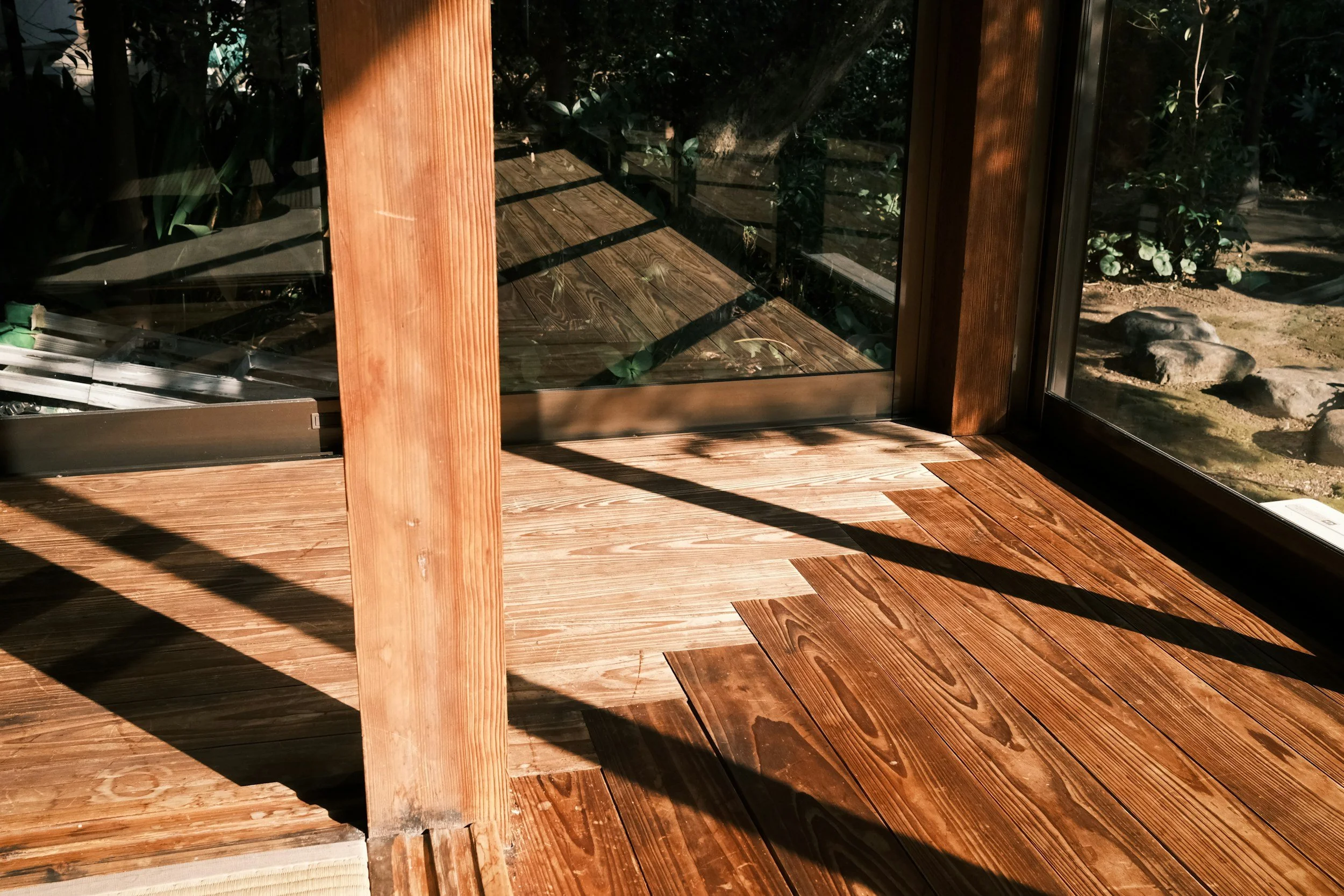 Close-up view of a wooden deck with glass panels and natural scenery of rocks and plants outside.