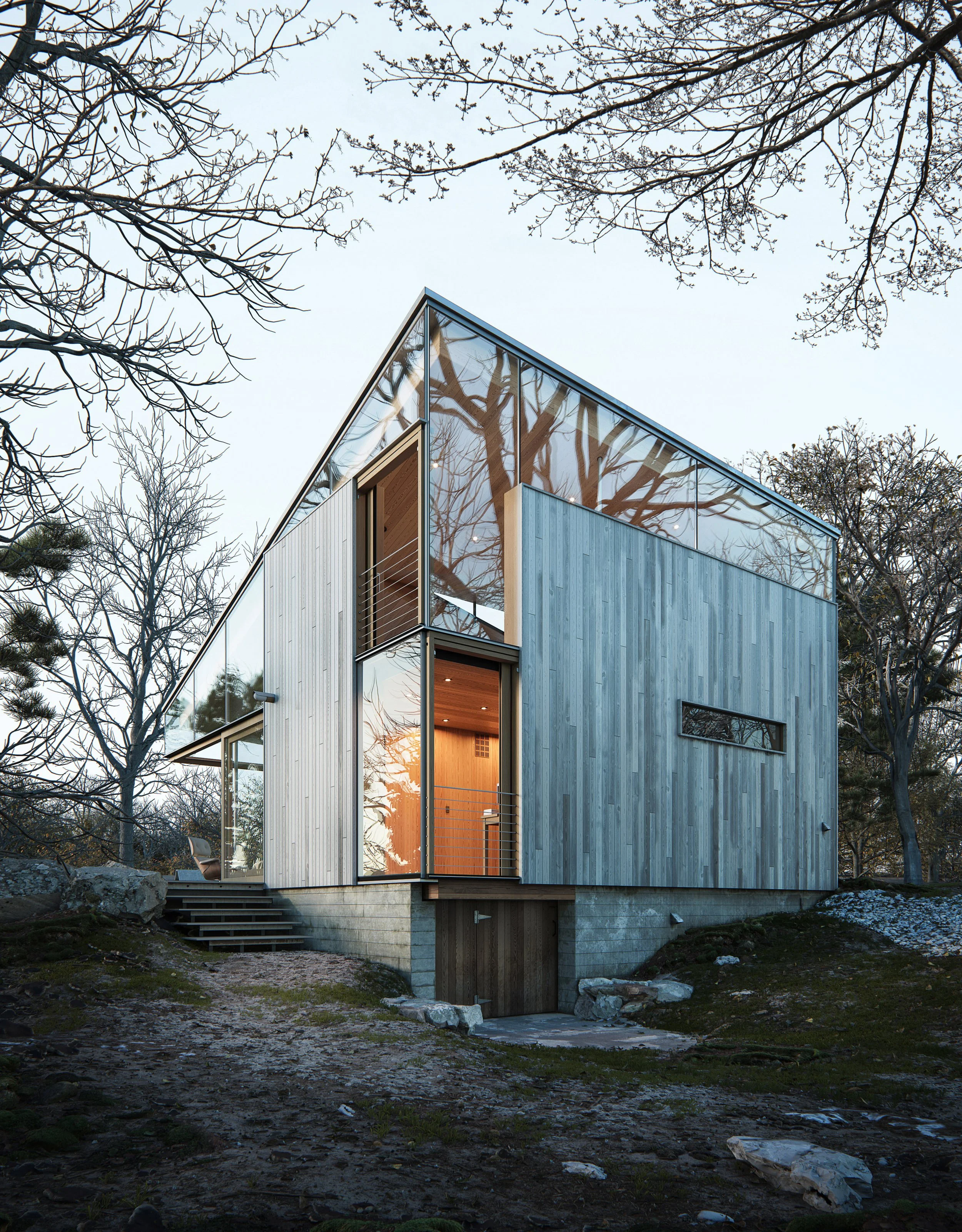Modern multi-story house with large glass windows and blue wooden exterior, set in a natural environment with leafless trees and rocky terrain, during dusk.