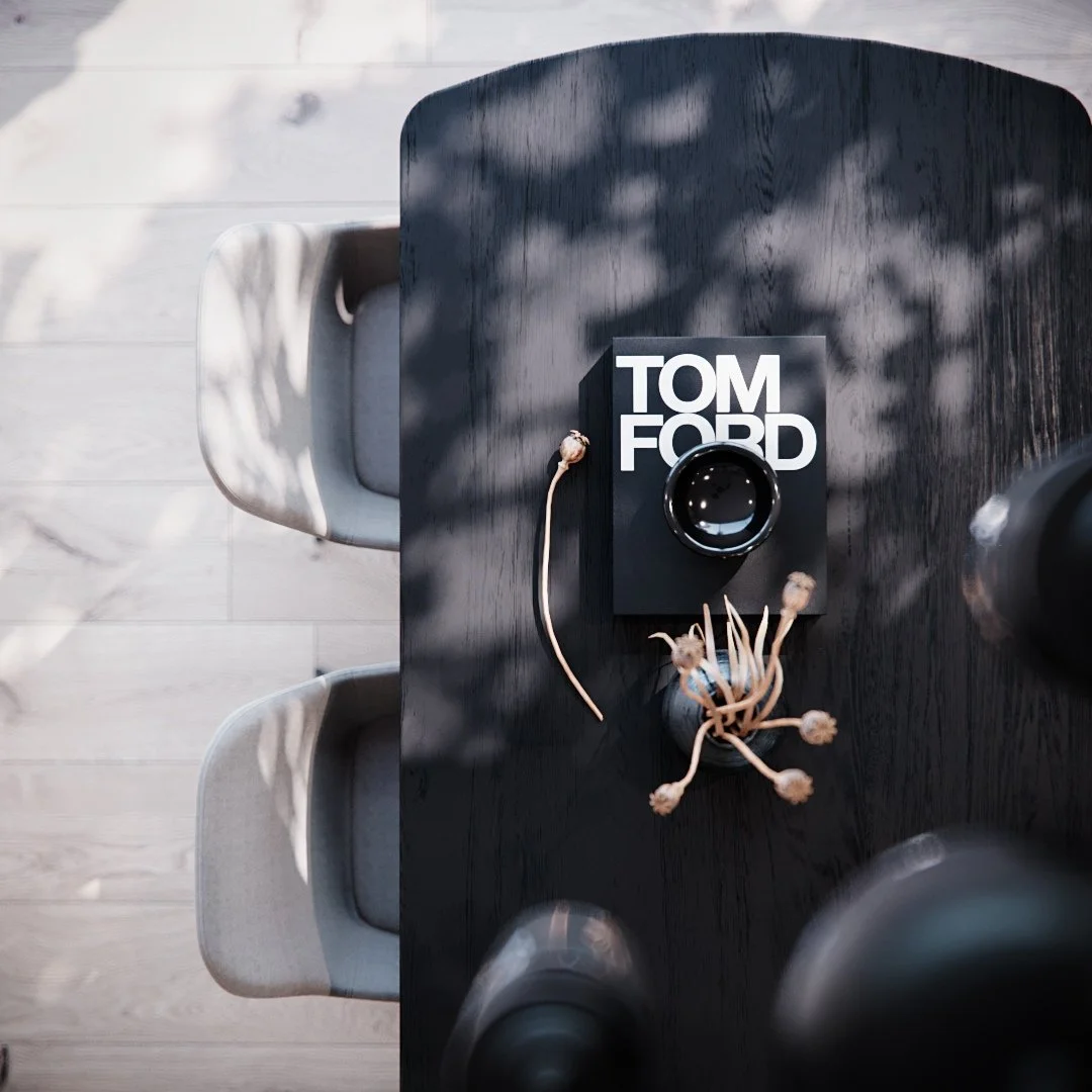 Top view of a black wooden table with a Tom Ford candle, dried plant stems, and chairs around it, with shadows of leaves cast on the surface.