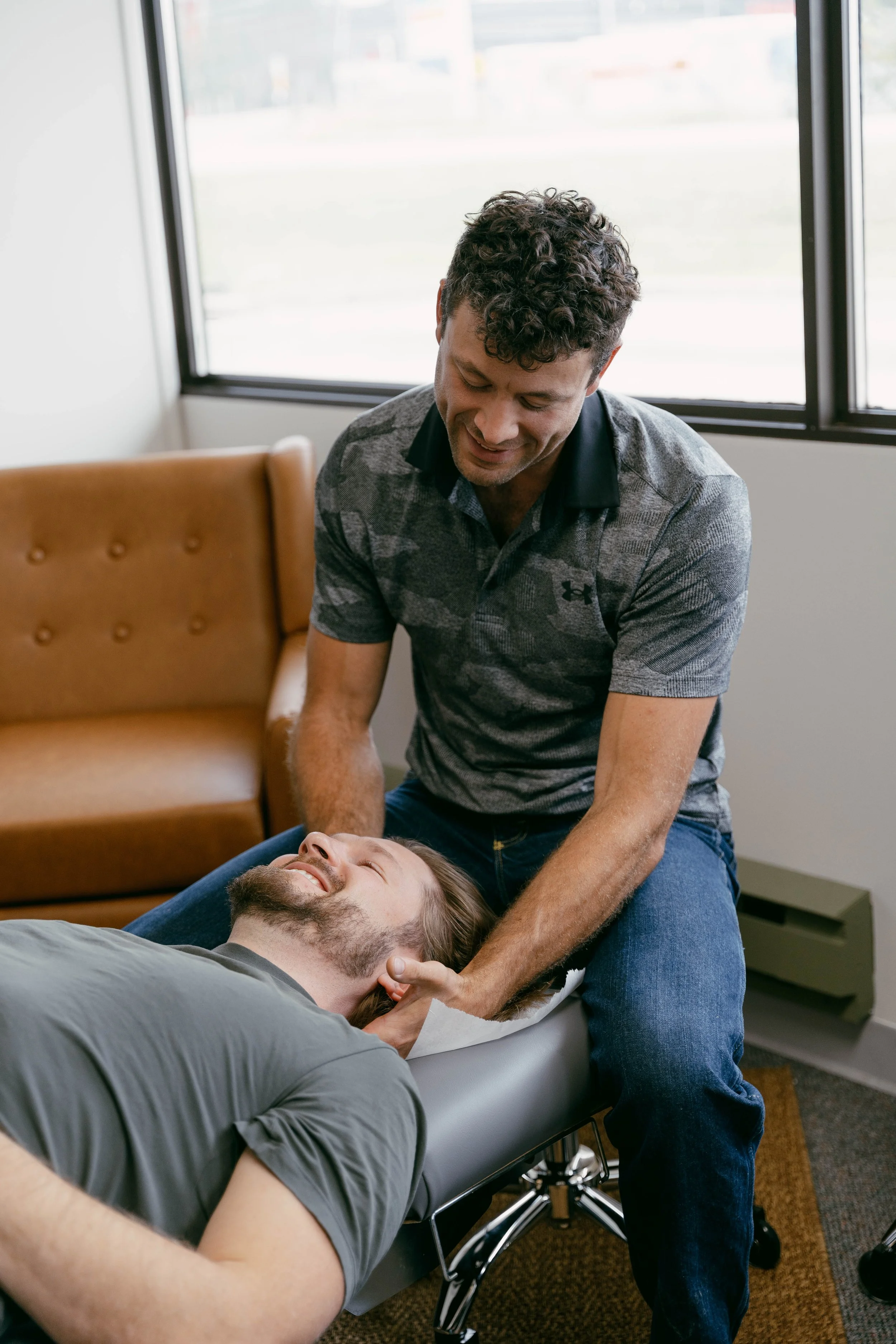 Man lying on a chiropractic adjustment table, smiling, while another man performs an adjustment on his neck.