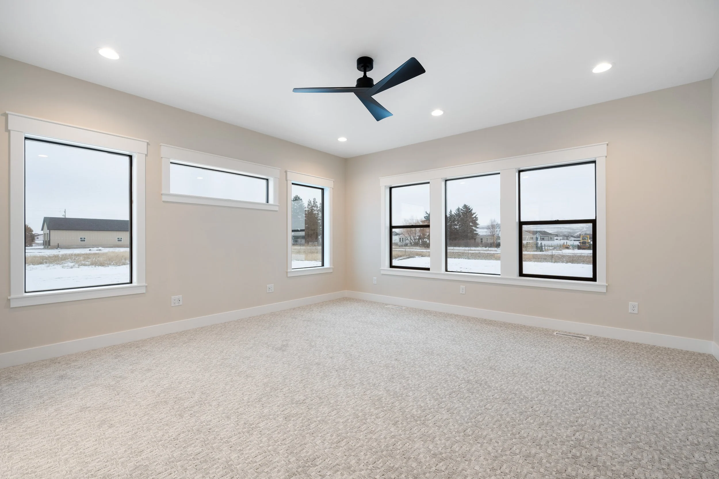 Carpeted living area with large windows and a ceiling fan — JAB Construction’s Timeless Craftsman custom home in Iona, Idaho.
