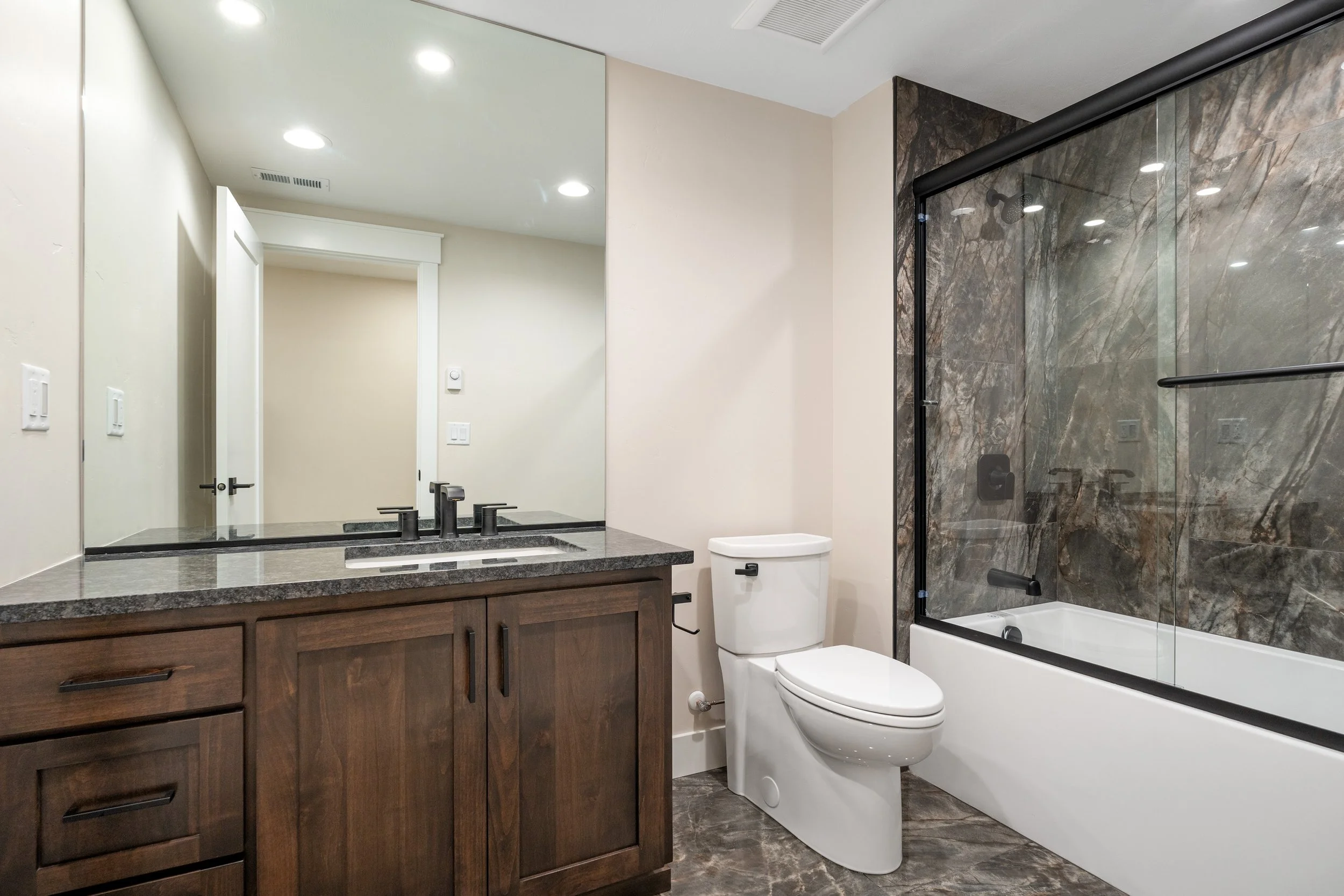 Bathroom with a dark wood vanity and patterned shower curtain — JAB Construction’s Timeless Craftsman custom home in Iona, Idaho.