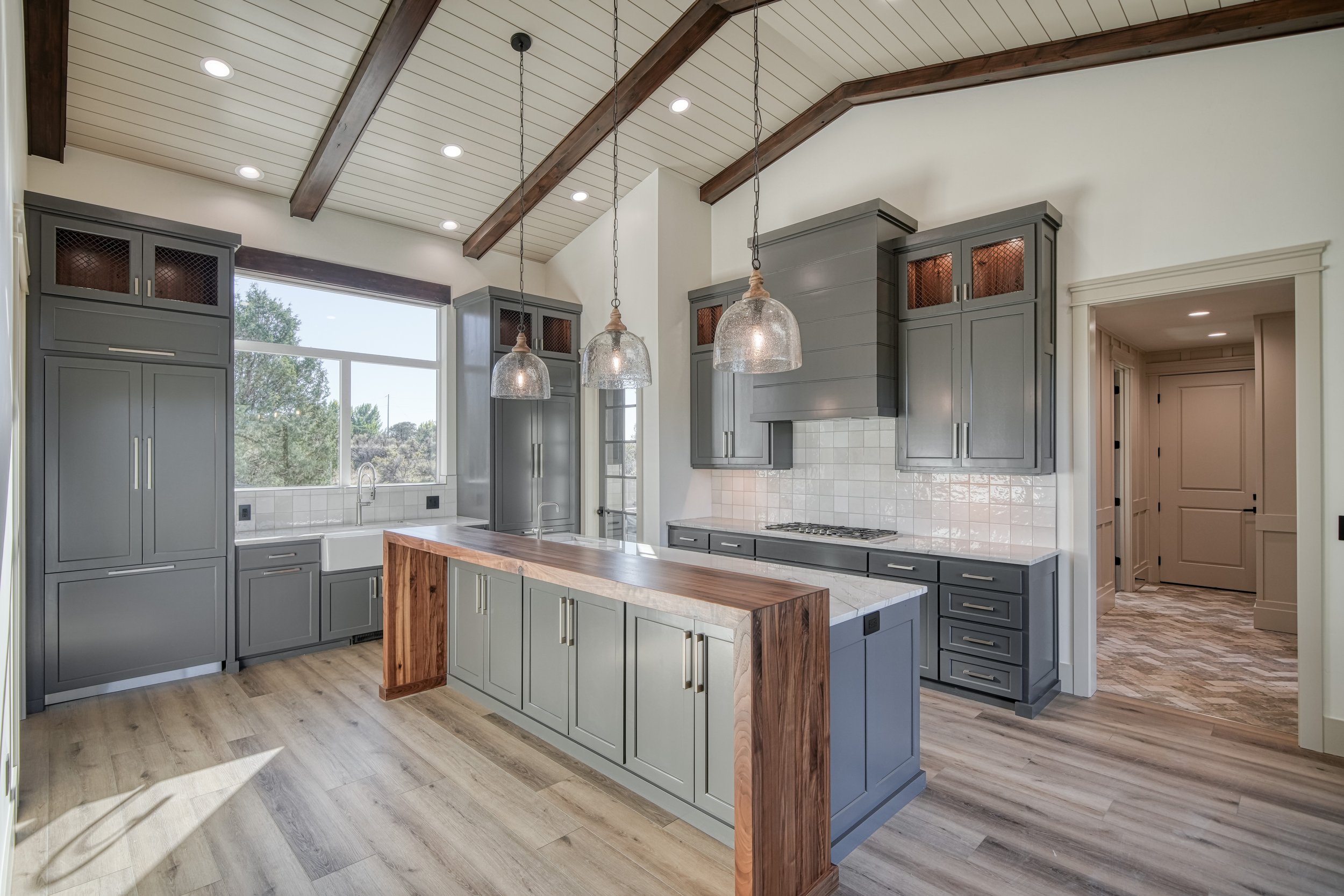 Kitchen with an island, pendant lights and exposed ceiling beams — JAB Construction’s Modern Transitional custom home in Blackfoot, Idaho.