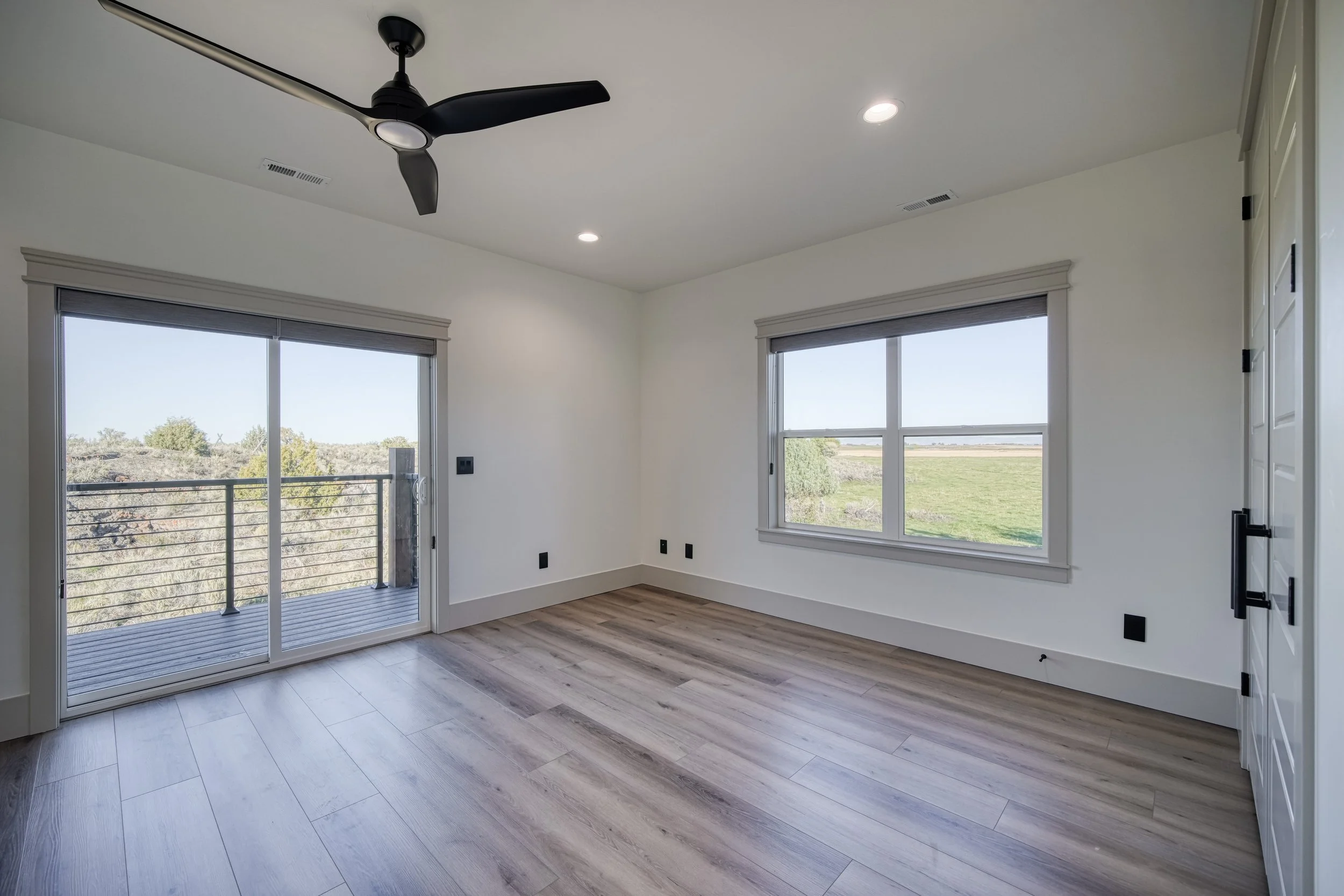 Room with wood-look flooring, large windows and a ceiling fan — JAB Construction’s Modern Transitional custom home in Blackfoot, Idaho.