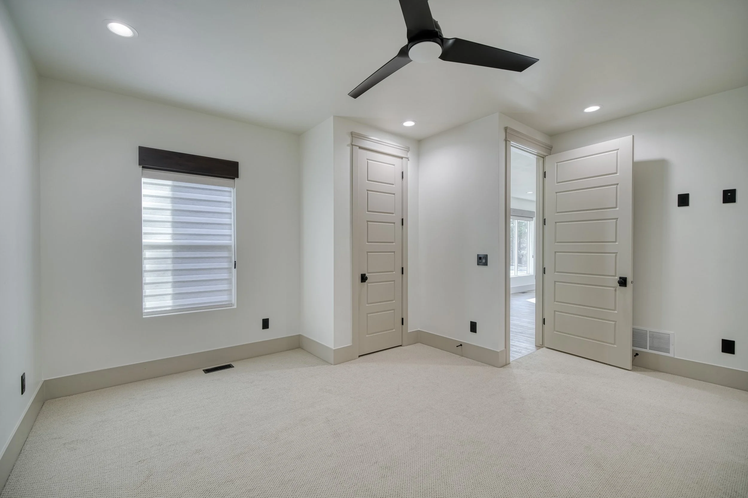 Carpeted bedroom with a ceiling fan and large windows — JAB Construction’s Modern Transitional custom home in Blackfoot, Idaho.