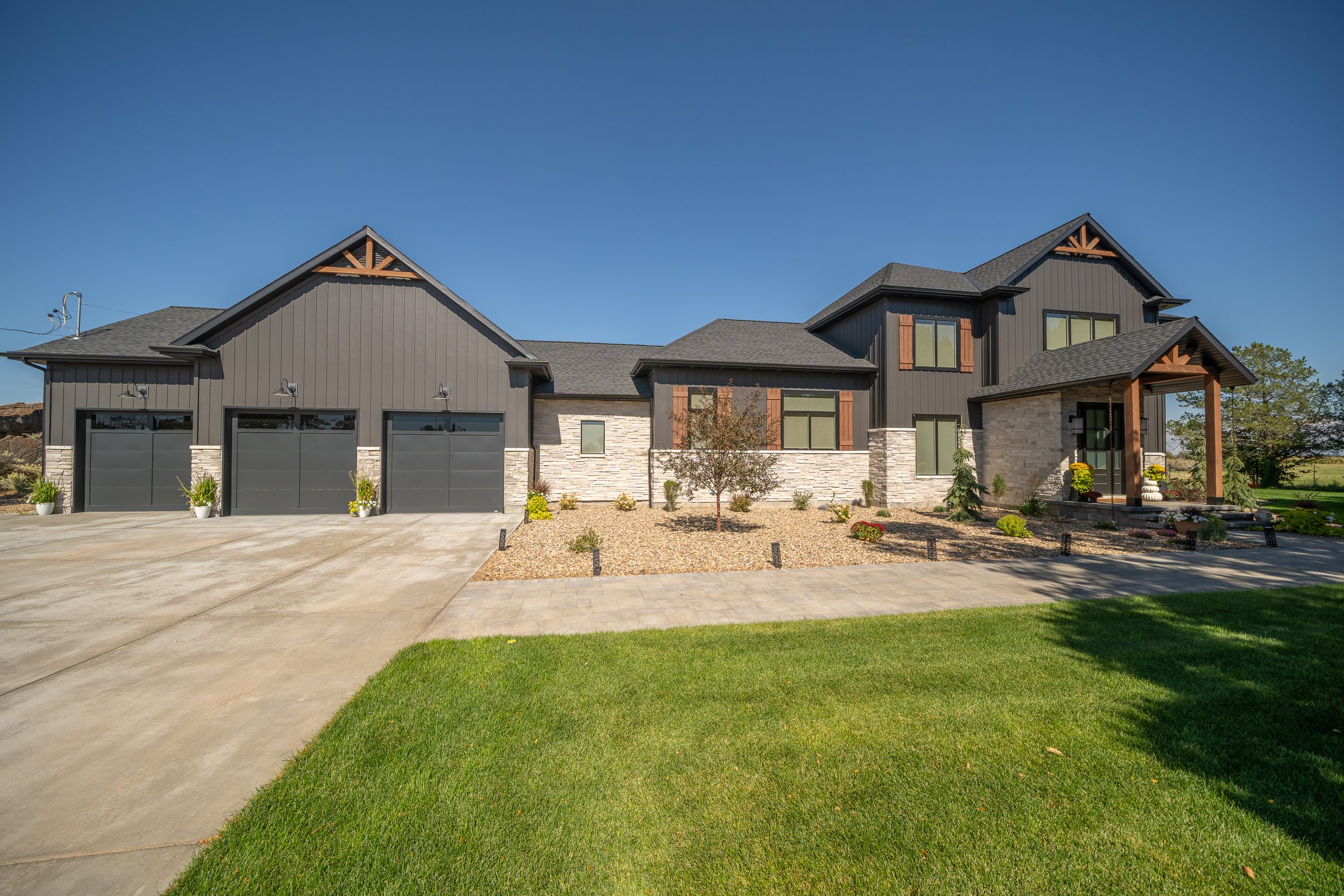 Home exterior with a landscaped lawn, dark siding and three-car garage — JAB Construction’s Modern Transitional custom home in Blackfoot, Idaho.