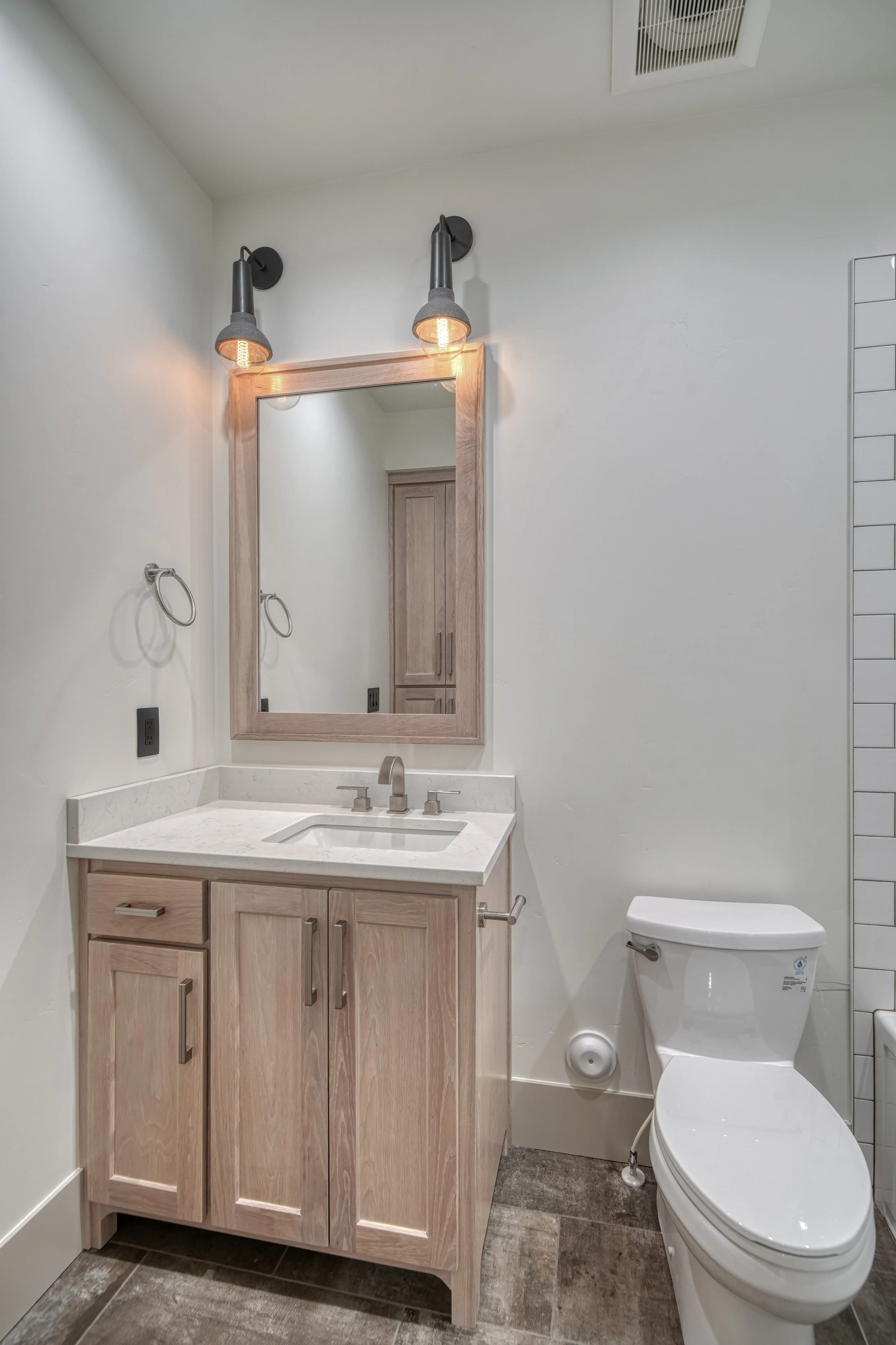 Bathroom with a wood vanity, framed mirror and toilet — JAB Construction’s Modern Transitional custom home in Blackfoot, Idaho.