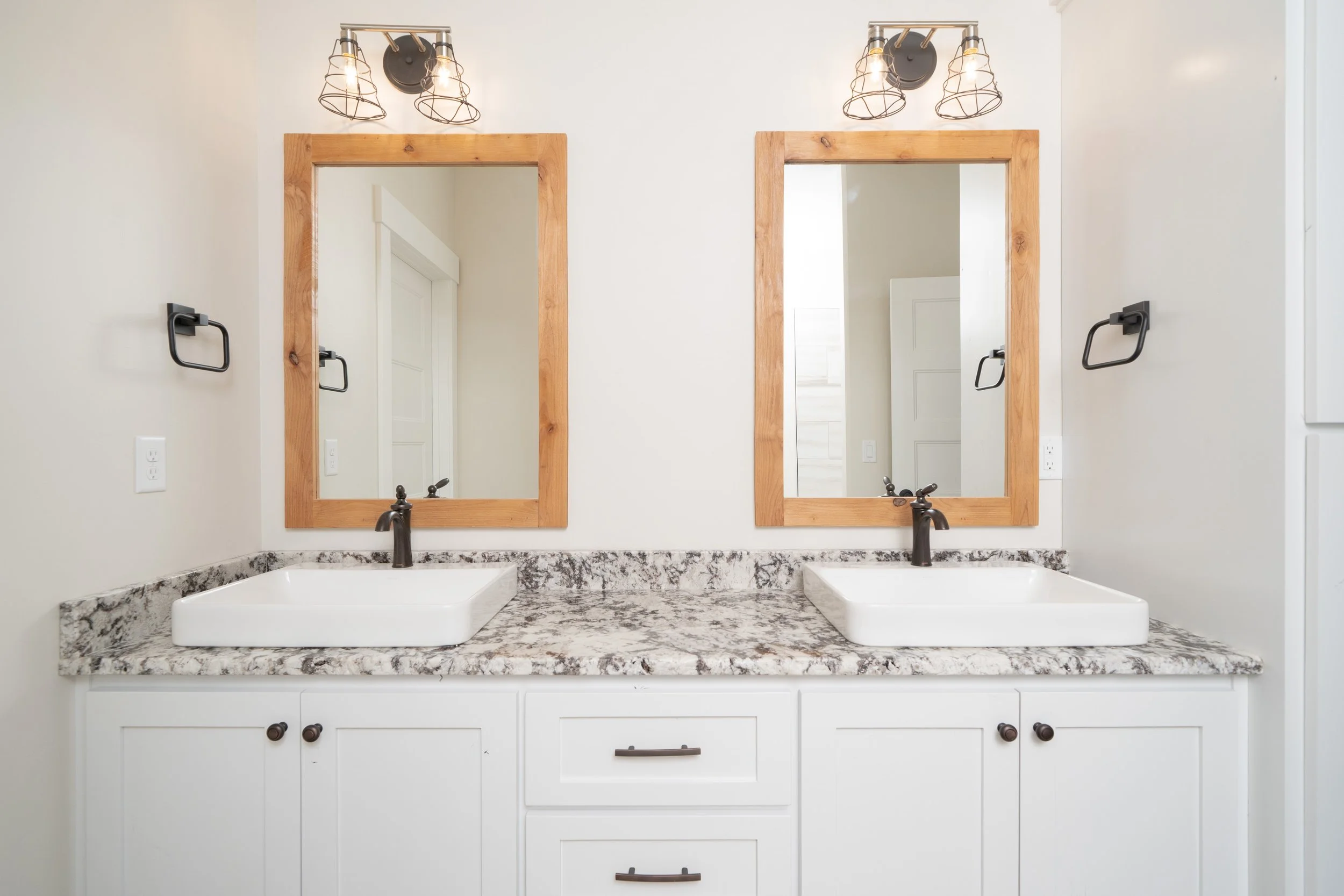 Bathroom vanity with double sinks, wood-framed mirrors and black light fixtures at JAB Construction’s Country Craftsman custom home in Shelley, Idaho.