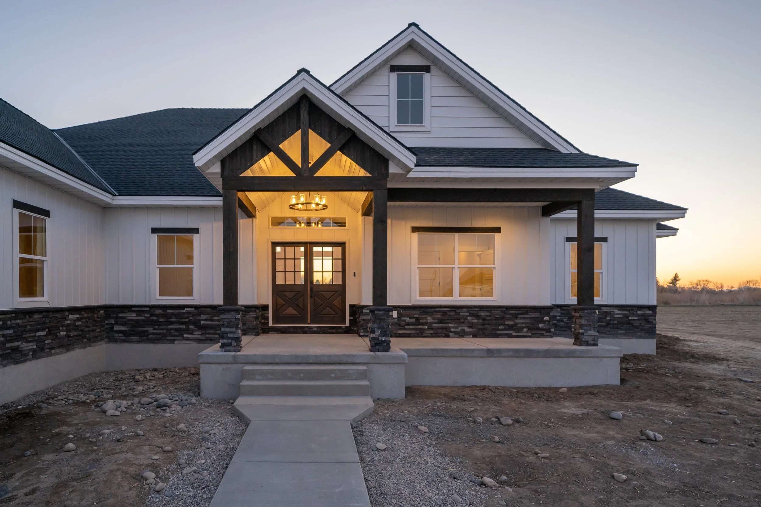 Home exterior at sunset with a porch and double front doors at JAB Construction’s Country Craftsman custom home in Shelley, Idaho.