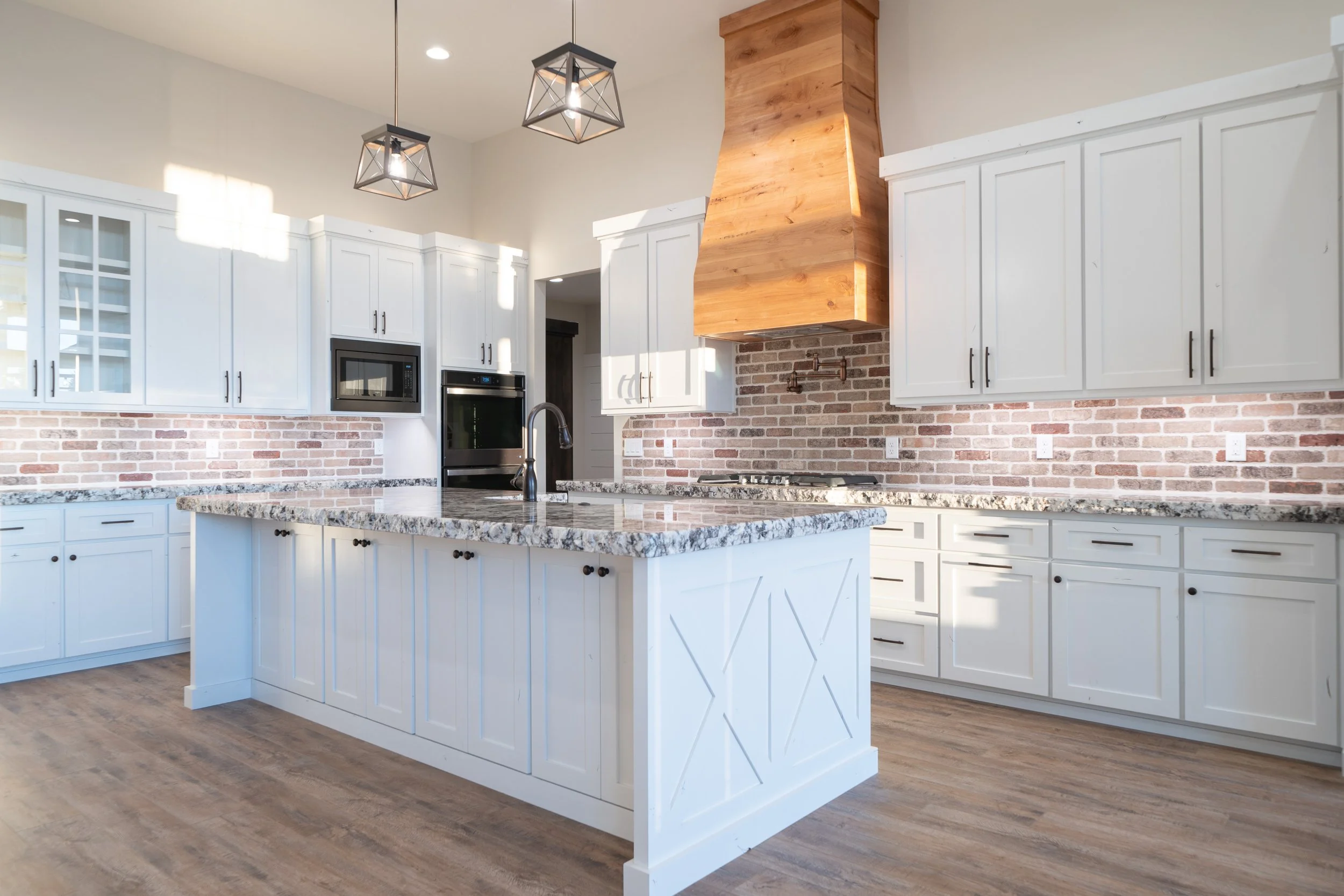 Kitchen with a large island, white cabinets and wood range hood at JAB Construction’s Country Craftsman custom home in Shelley, Idaho.