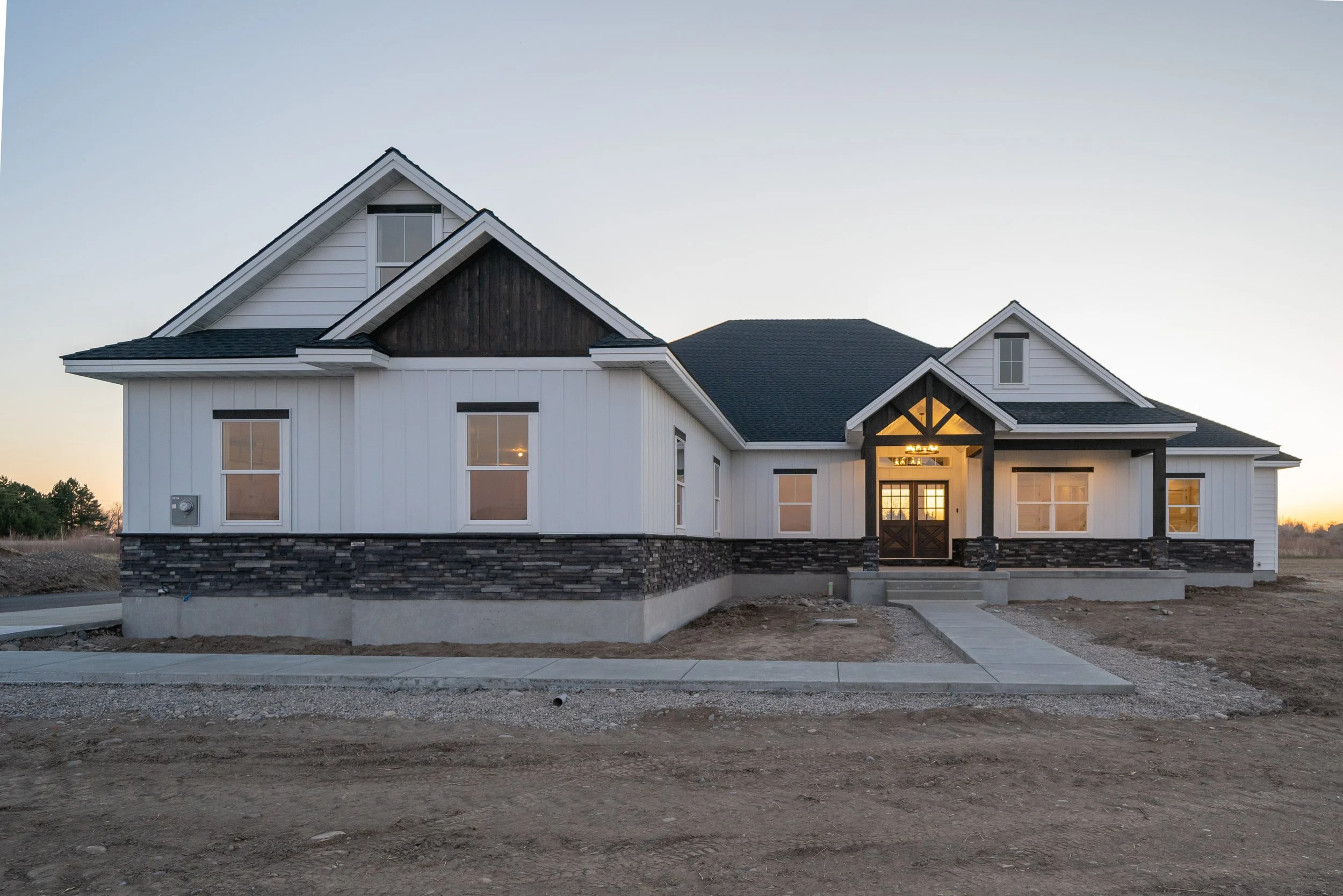 White home exterior at dusk with dark roofing and front steps at JAB Construction’s Country Craftsman custom home in Shelley, Idaho.