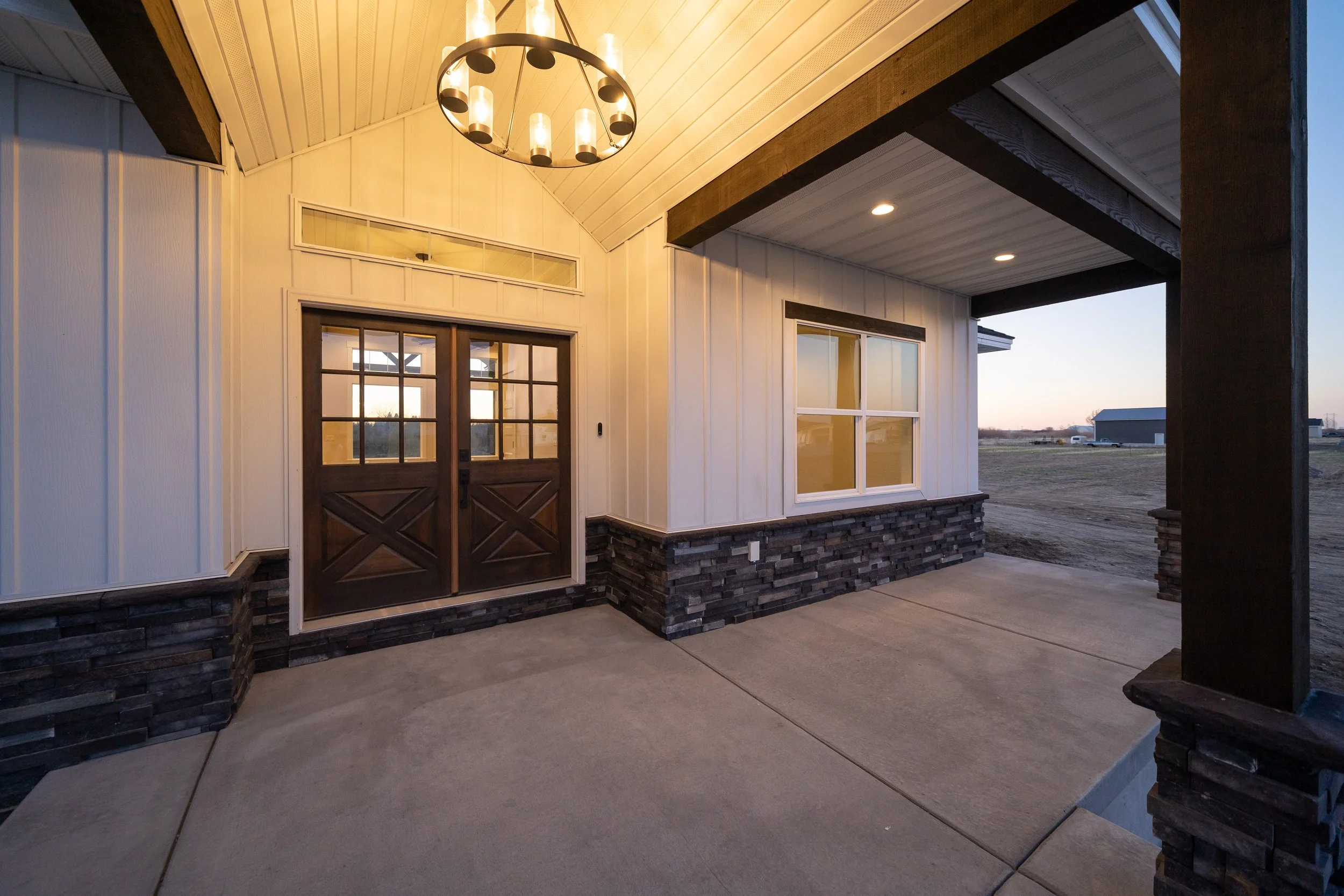 Covered front porch with double wood doors and timber beams at JAB Construction’s Country Craftsman custom home in Shelley, Idaho.