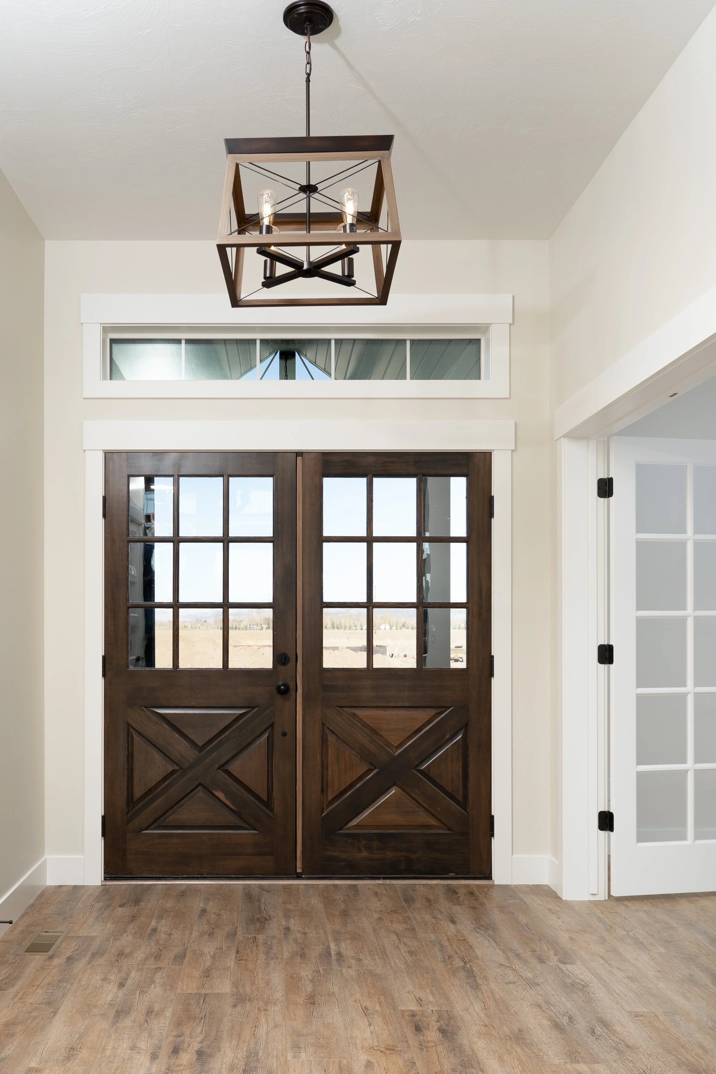 Entryway with glass-paneled double doors and a chandelier at JAB Construction’s Country Craftsman custom home in Shelley, Idaho.