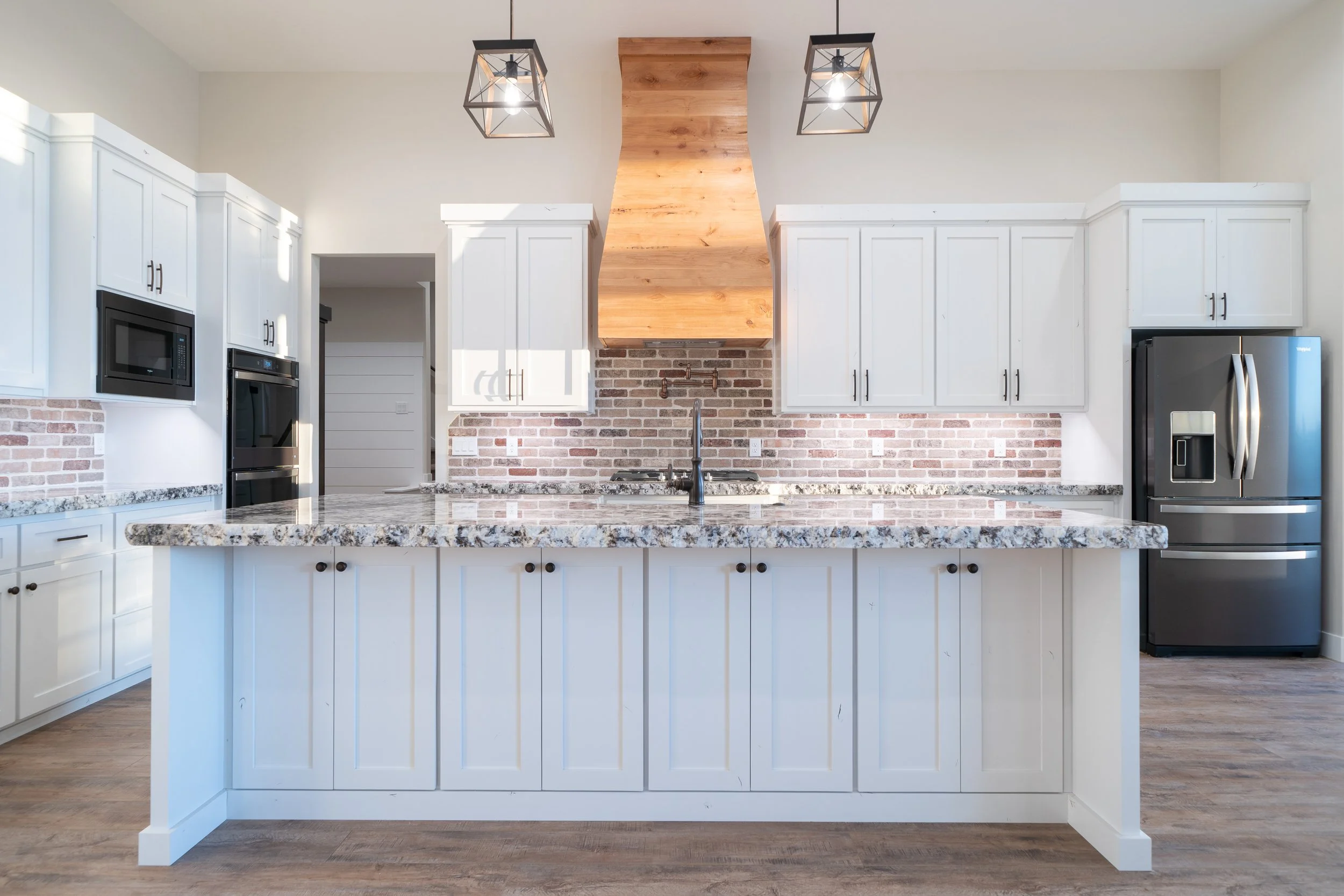 Kitchen with white cabinets, an island, a wood range hood and pendant lights at JAB Construction’s Country Craftsman custom home in Shelley, Idaho.
