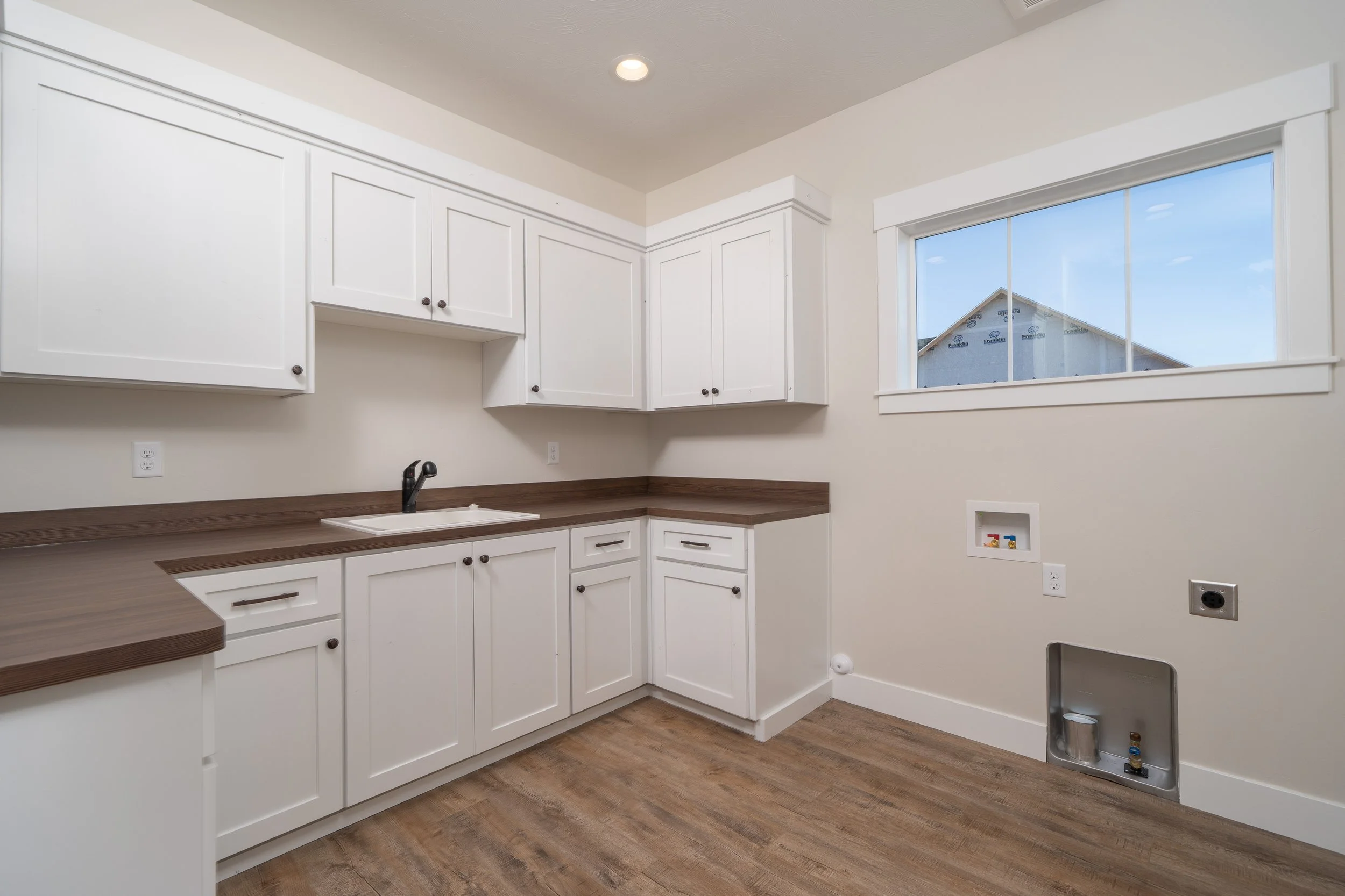 Kitchen with white cabinets, a large window and wood-look flooring at JAB Construction’s Country Craftsman custom home in Shelley, Idaho.