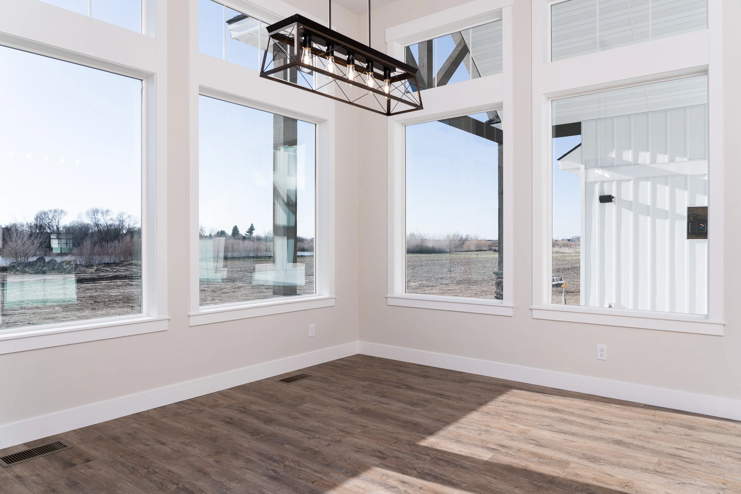 Room with large windows, wood flooring and an exposed-bulb ceiling light at JAB Construction’s Country Craftsman custom home in Shelley, Idaho.