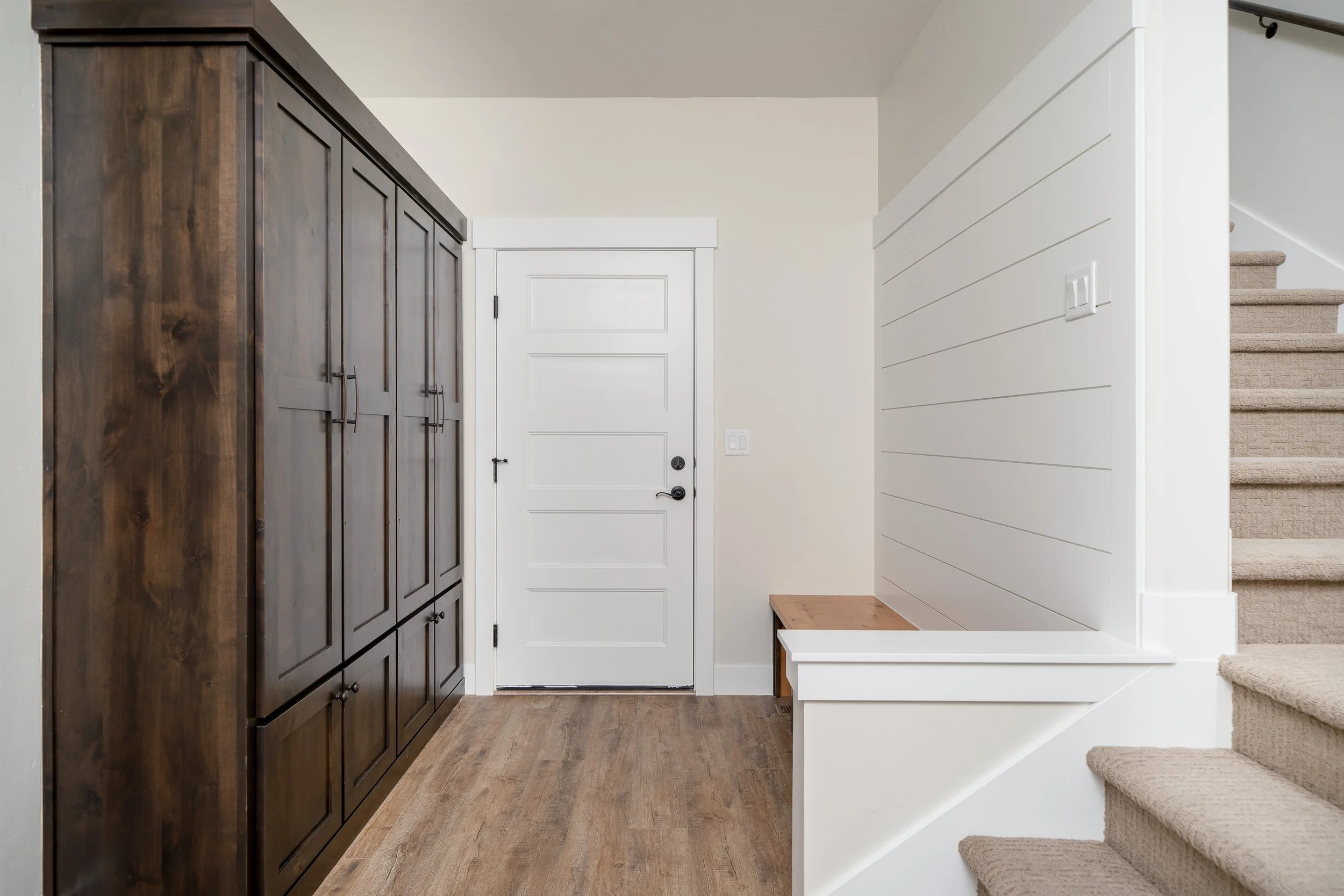 Entryway with wood cabinets, a white door and carpeted stairs at JAB Construction’s Country Craftsman custom home in Shelley, Idaho.
