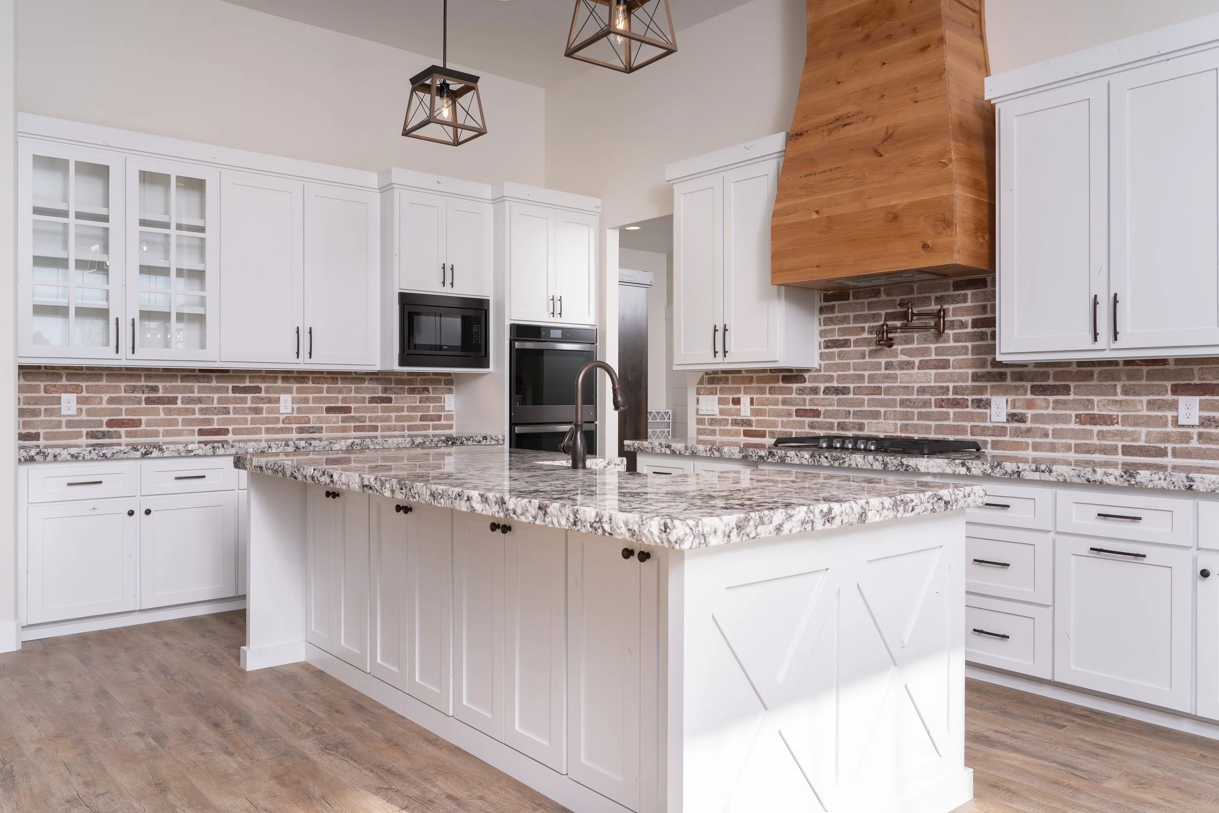 Kitchen island with white cabinetry, brick backsplash and pendant lights at JAB Construction’s Country Craftsman custom home in Shelley, Idaho.
