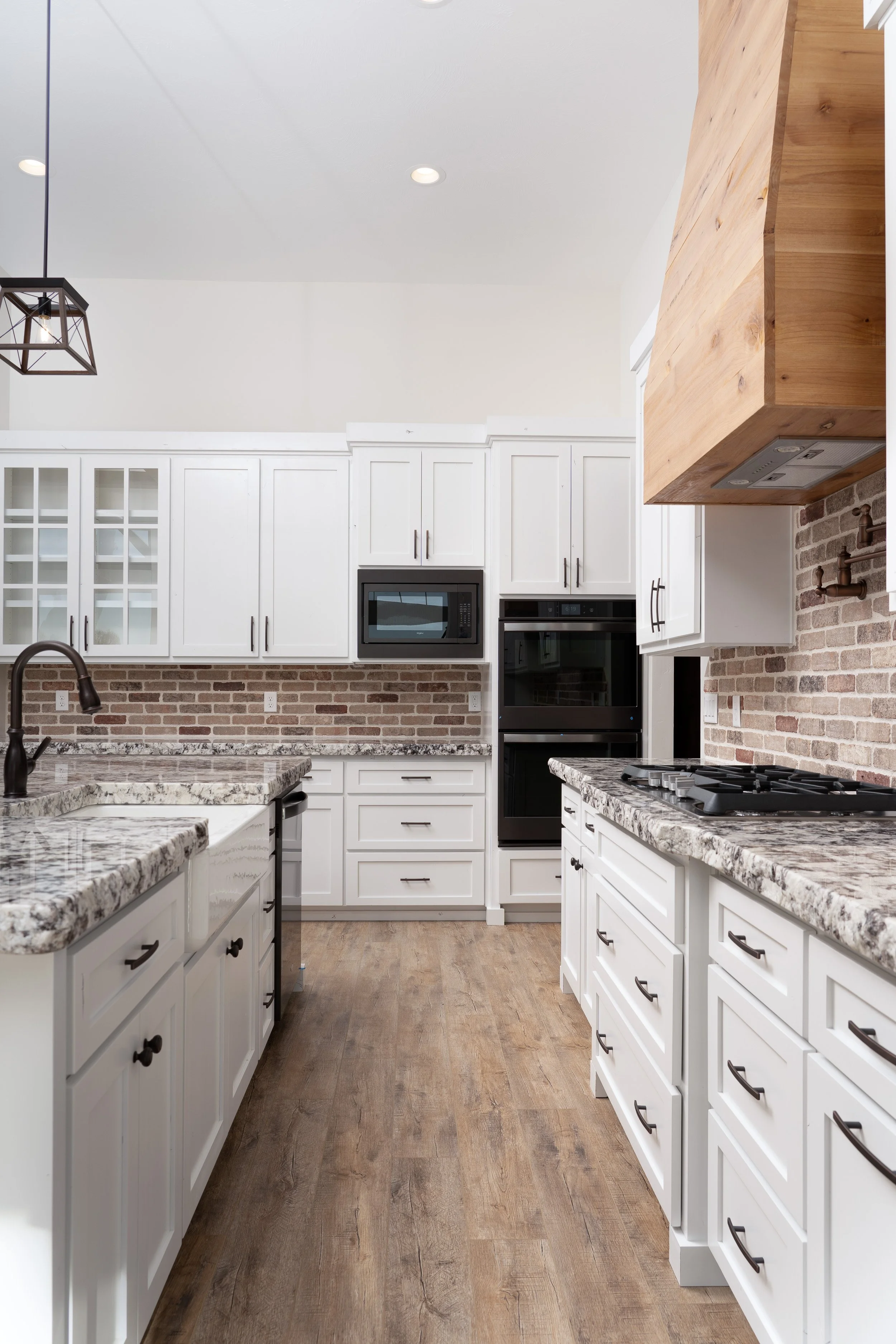 Kitchen with white cabinets, brick accents and a wood range hood at JAB Construction’s Country Craftsman custom home in Shelley, Idaho.