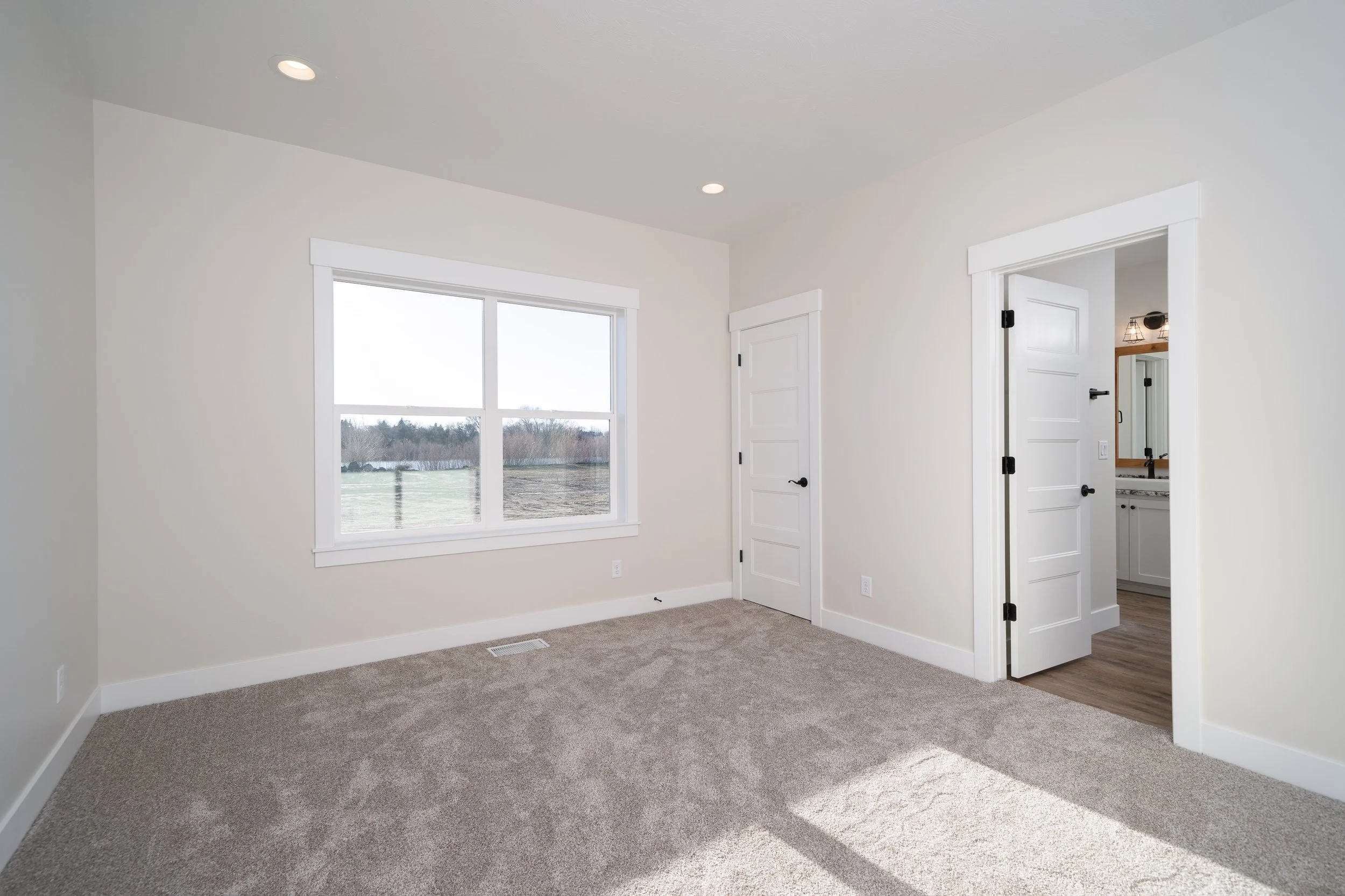 Carpeted room with a large window and adjoining doorways at JAB Construction’s Country Craftsman custom home in Shelley, Idaho.