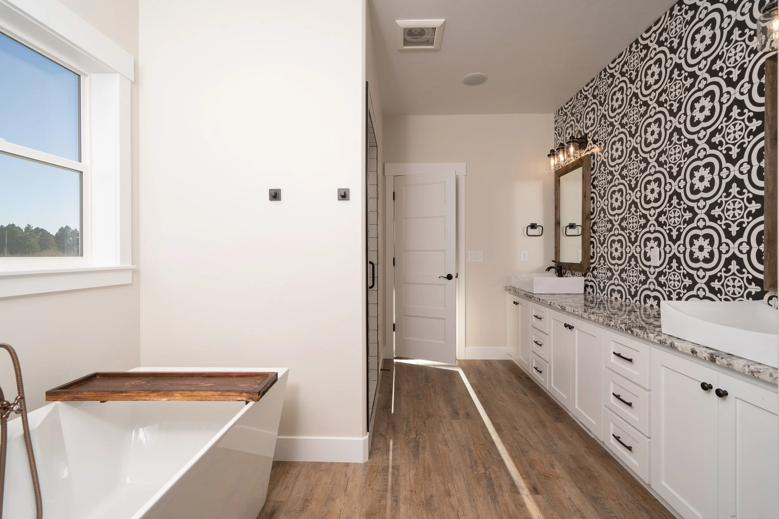 Bathroom with a freestanding tub, white vanity and patterned accent wall at JAB Construction’s Country Craftsman custom home in Shelley, Idaho.