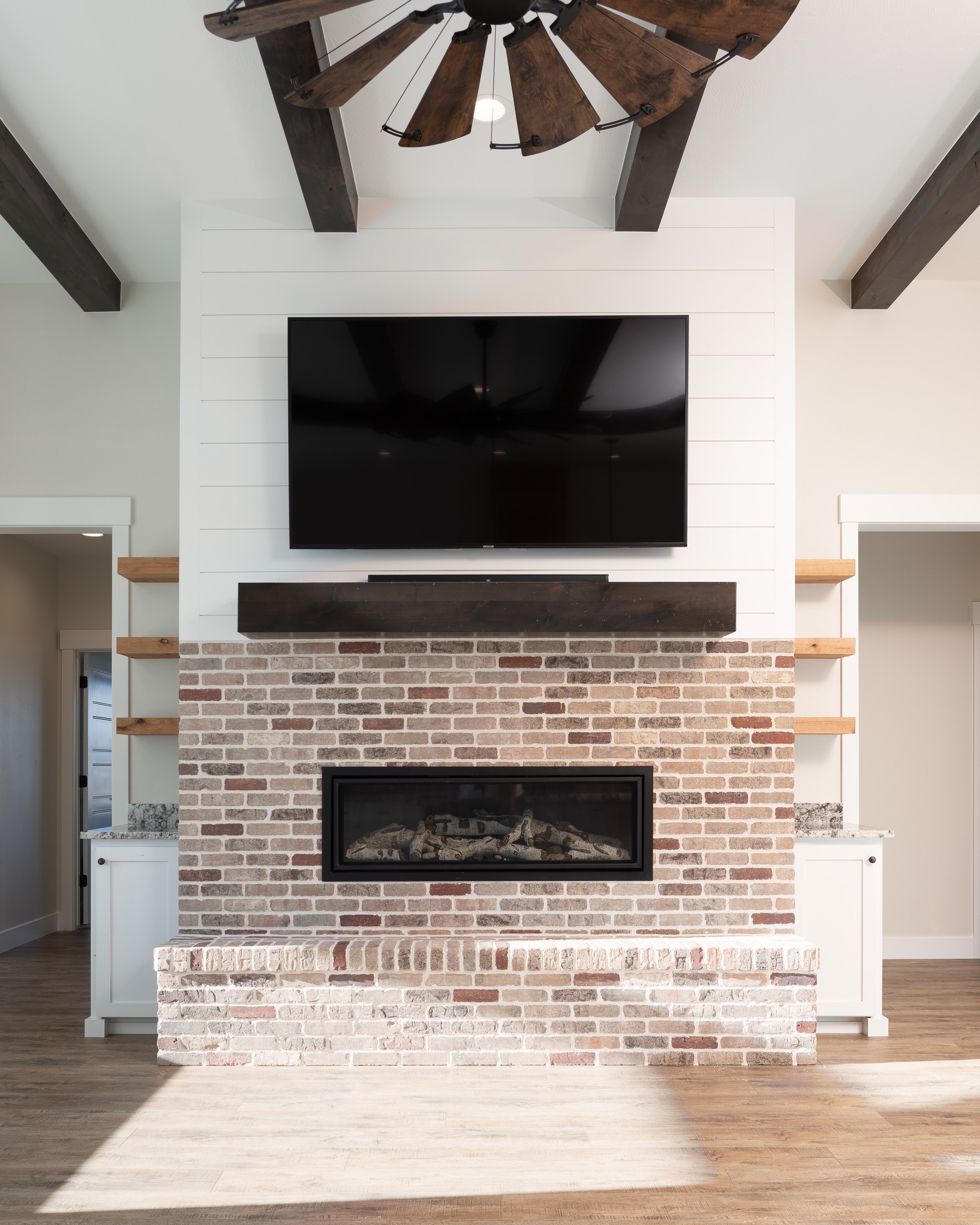 Brick fireplace with a wall-mounted TV and wood ceiling beams at JAB Construction’s Country Craftsman custom home in Shelley, Idaho.