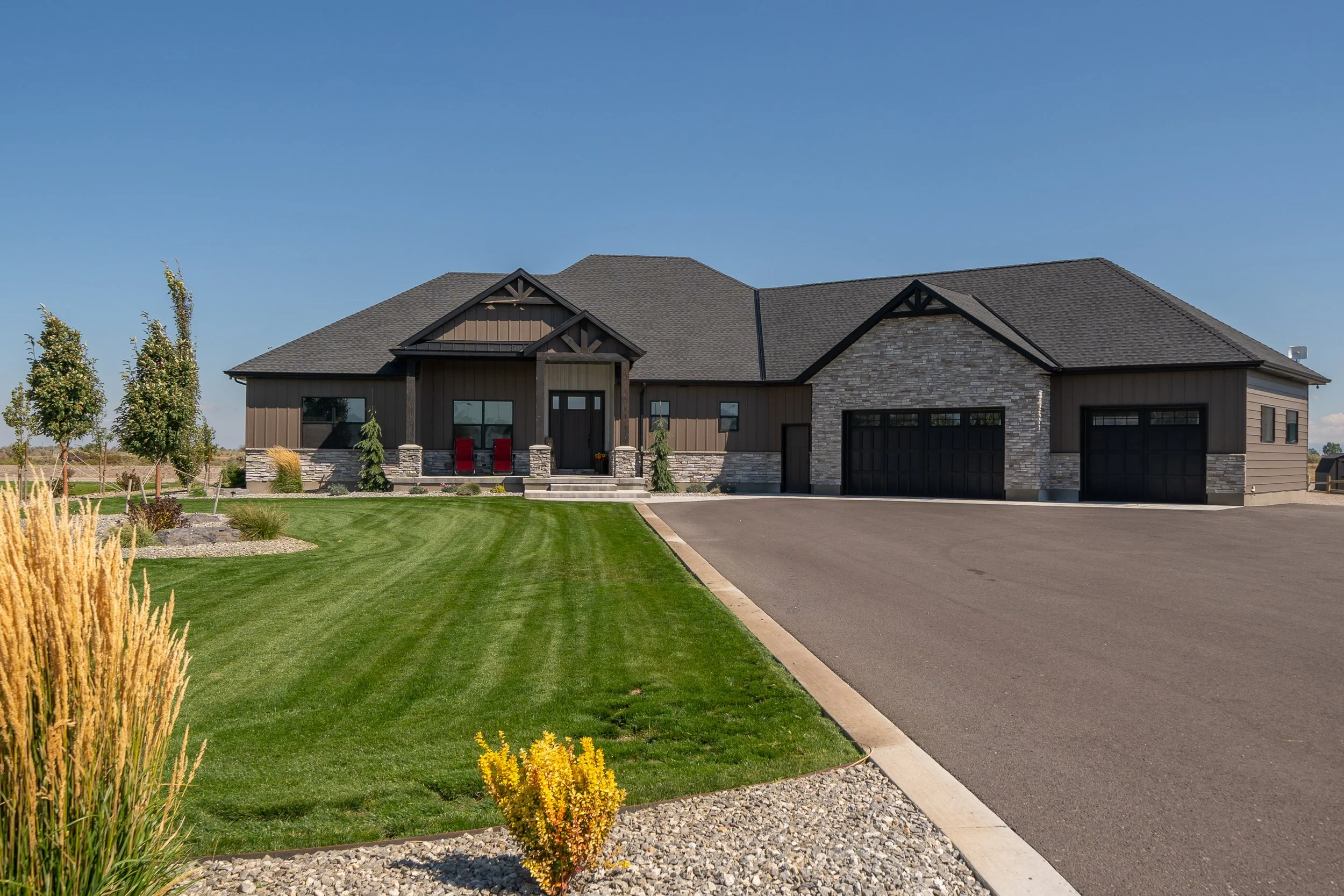 Home exterior with stone accents, landscaped lawn and three-car garage — JAB Construction’s Stone Craftsman custom home in Roberts, Idaho.