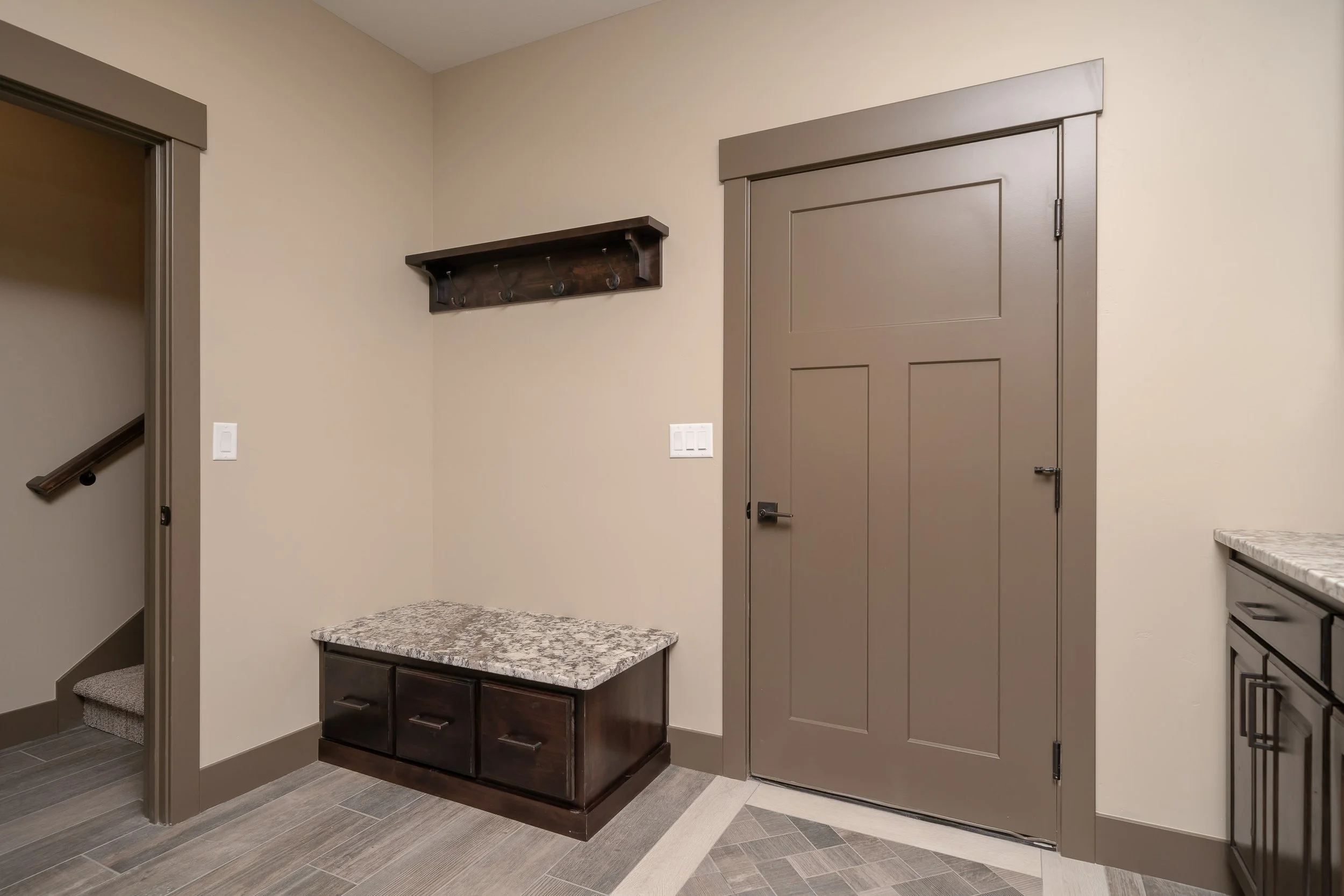 Entry bench with coat hooks beside a dark door — JAB Construction’s Stone Craftsman custom home in Roberts, Idaho.