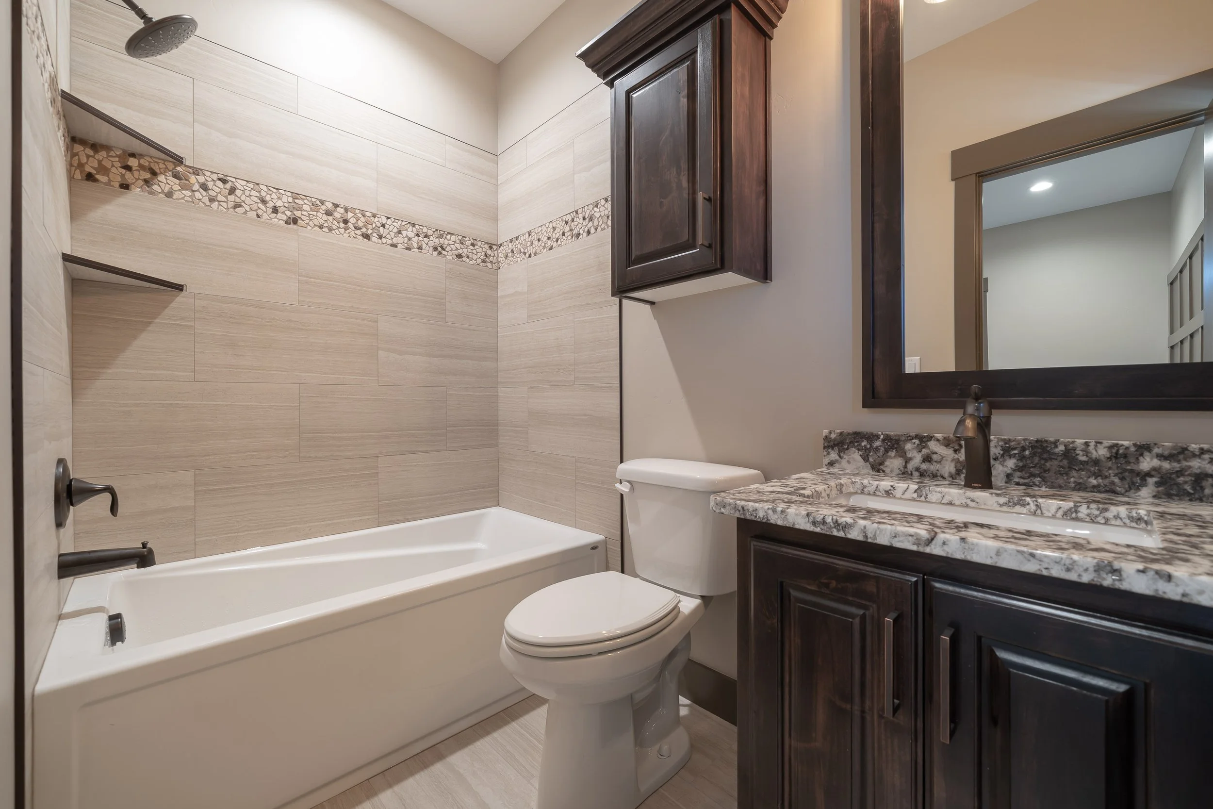 Bathroom with a tub, toilet and dark vanity — JAB Construction’s Stone Craftsman custom home in Roberts, Idaho.