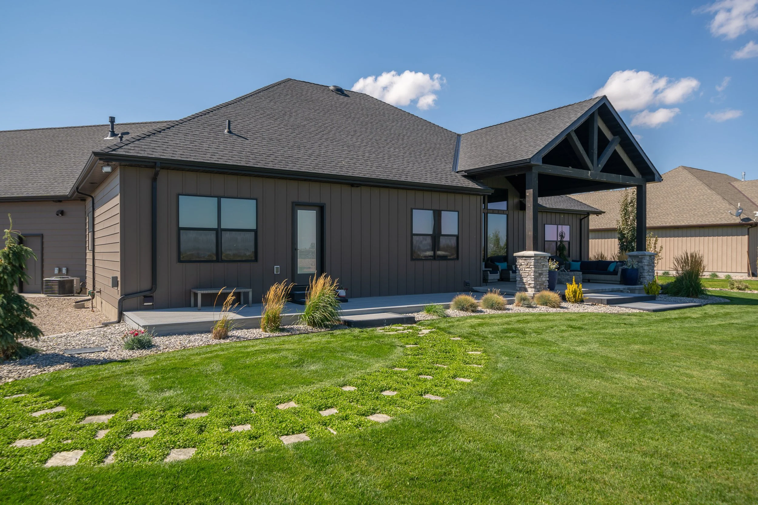 Rear home exterior beside a green lawn — JAB Construction’s Stone Craftsman custom home in Roberts, Idaho.